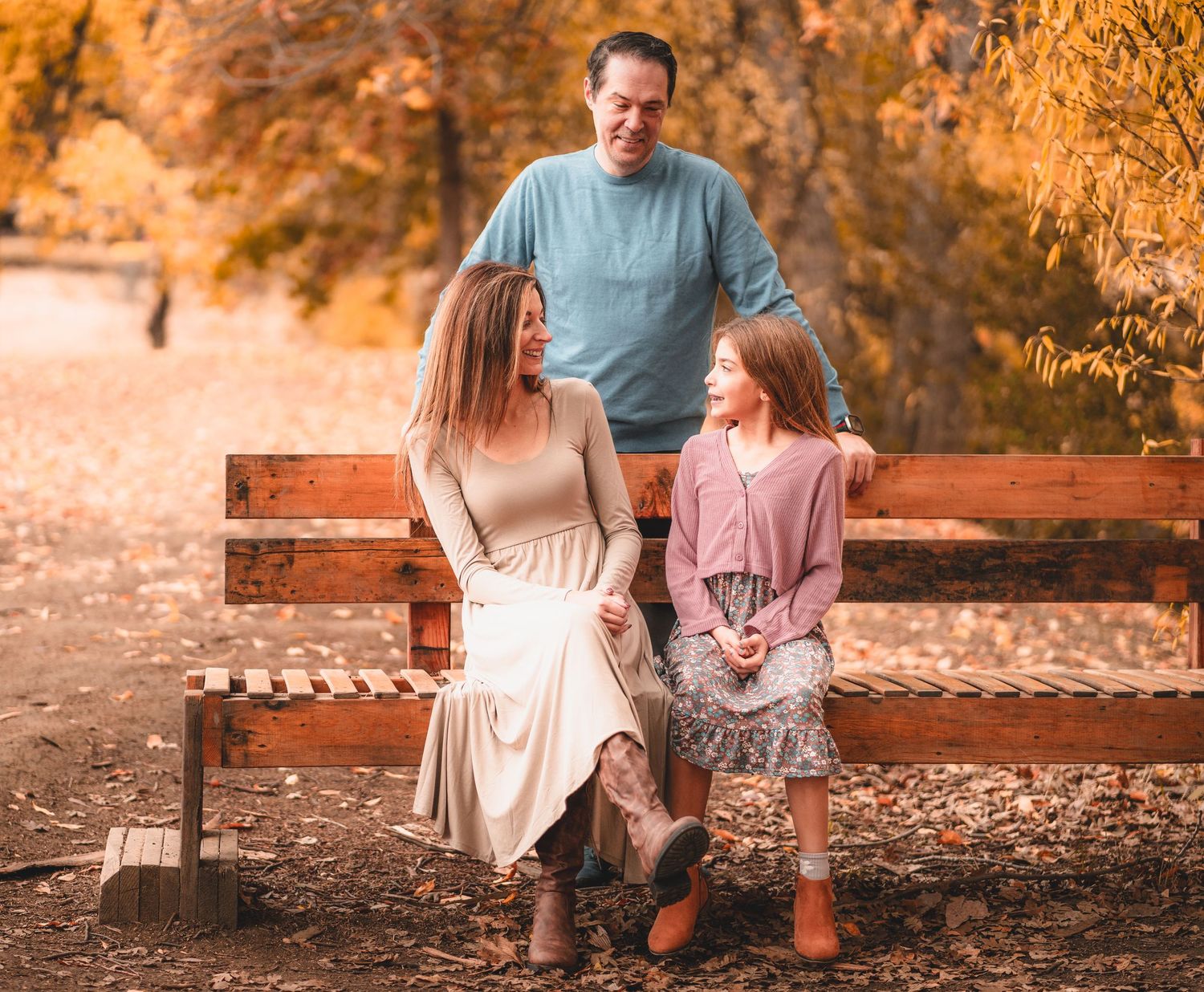 A family walks together on fallen autumn leaves in a park during golden hour.