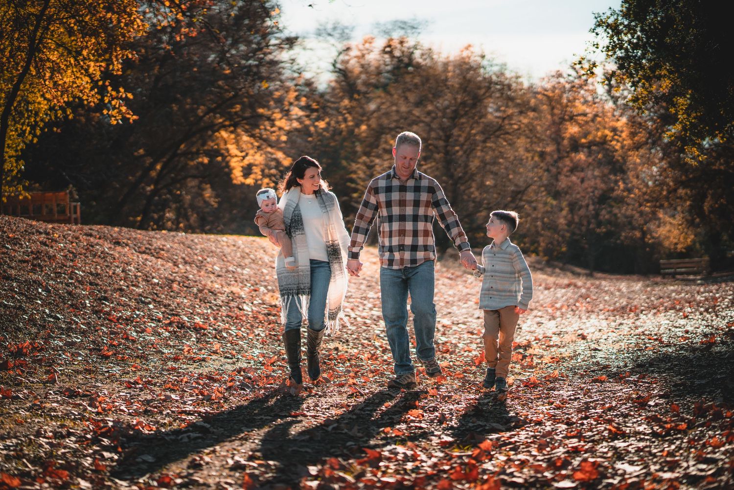 People strolling along a path covered in orange fall leaves during golden hour.