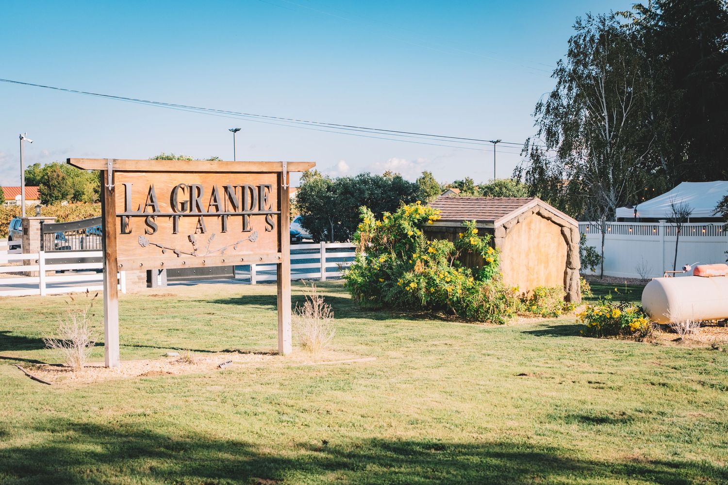 Rustic wooden La Grande Estate sign in front of a rural property with white fencing La Grande Estates