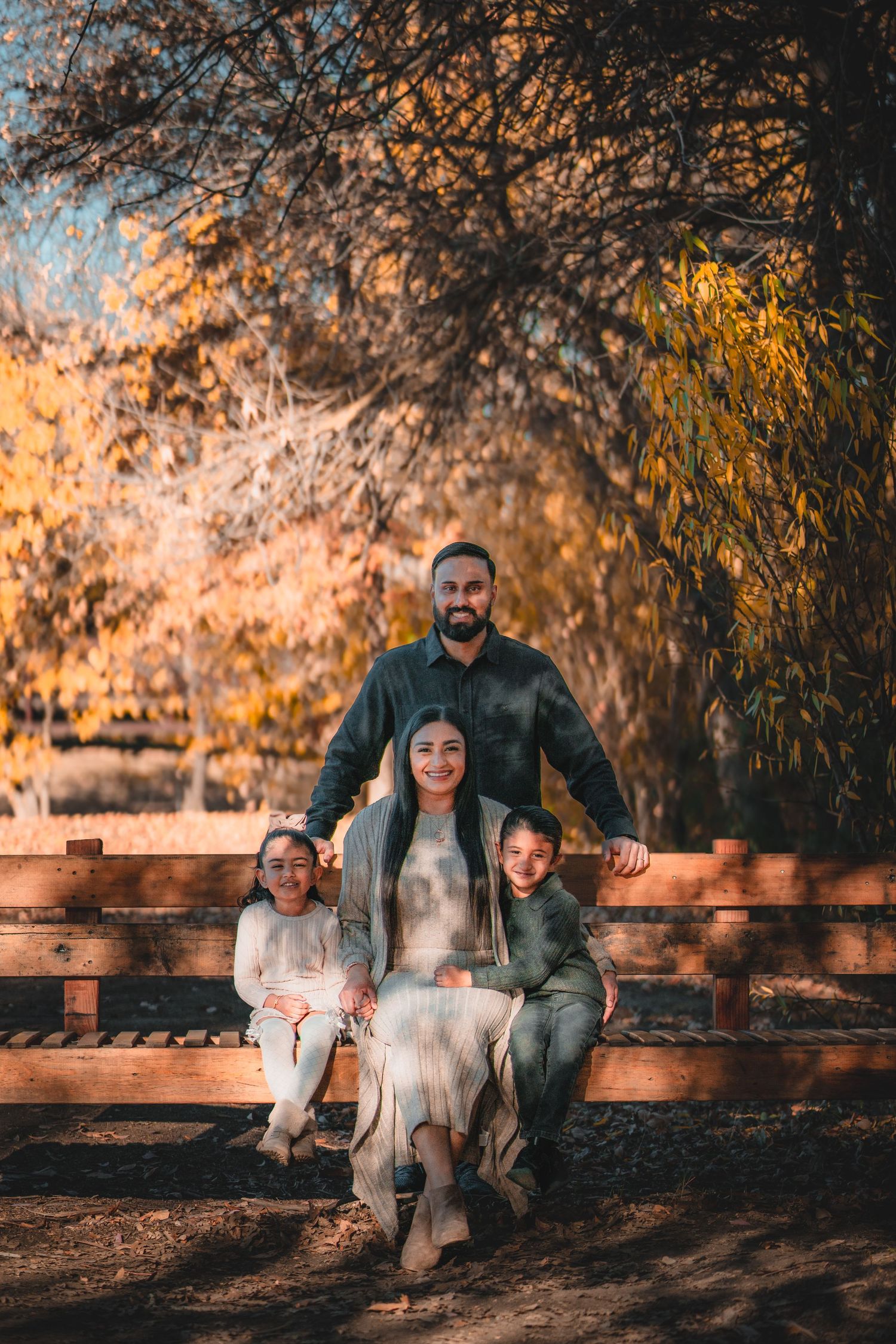 Family sitting together on wooden bench in park during fall season.