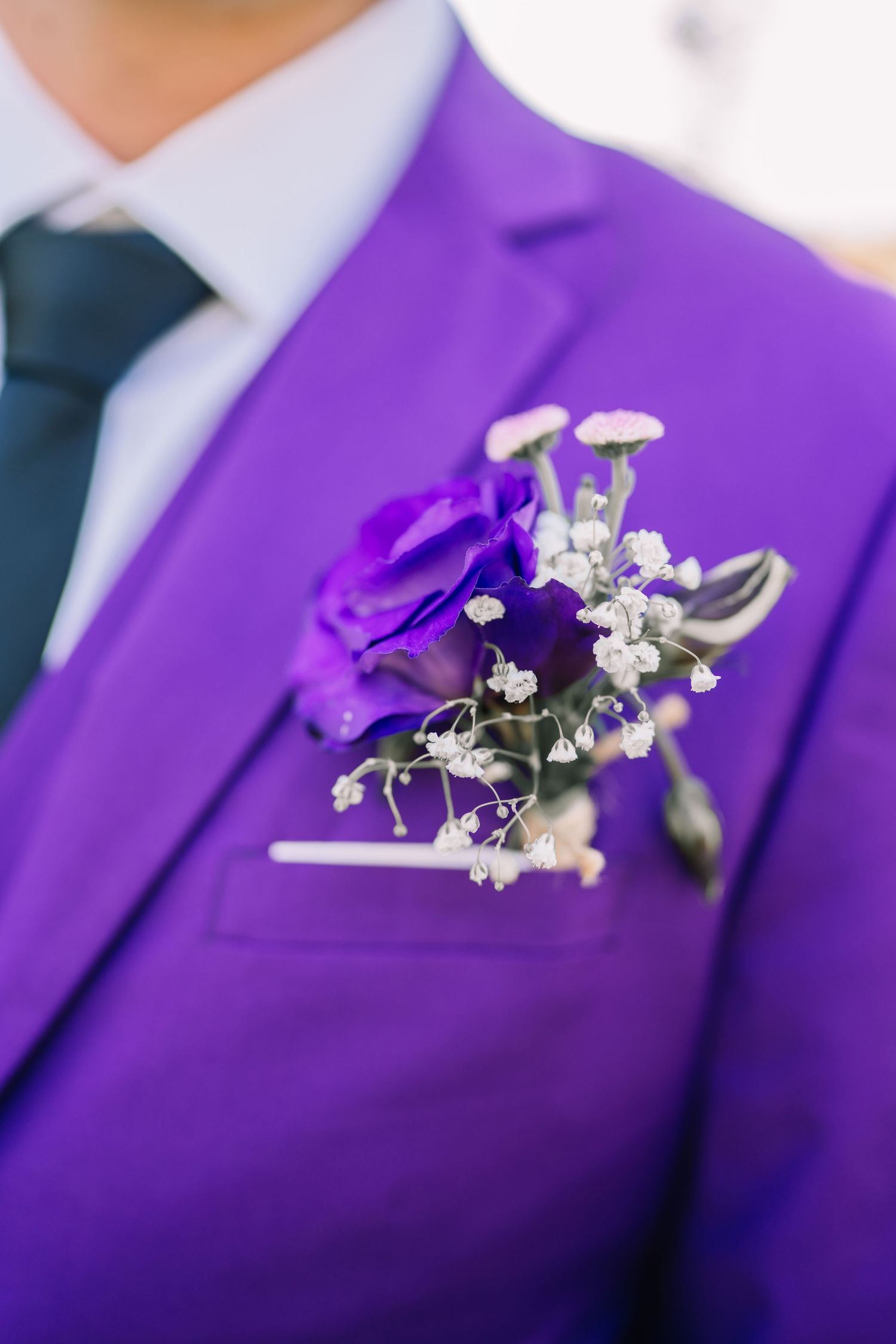 Man in purple suit with matching boutonniere featuring purple rose and white baby's breath on lapel.