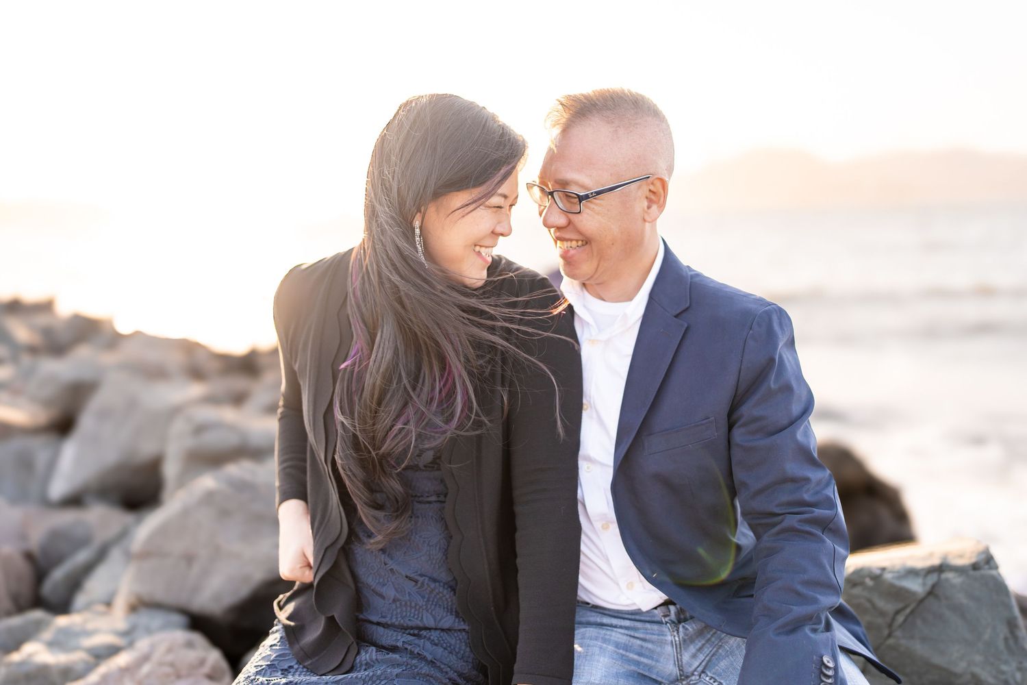 A couple shares intimate moments on a rocky beach at sunset.