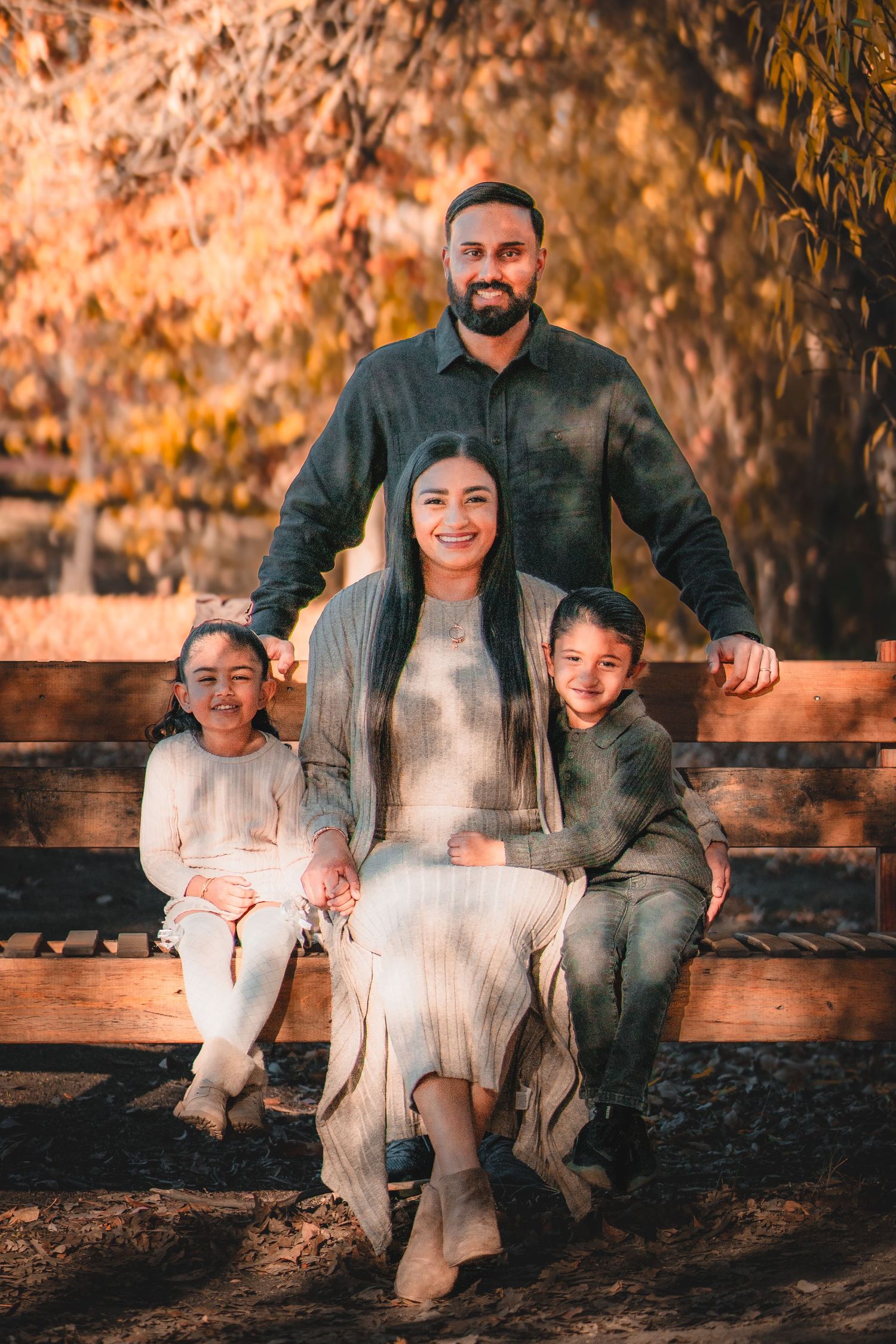 Family sitting together on a wooden bench surrounded by warm autumn lighting.