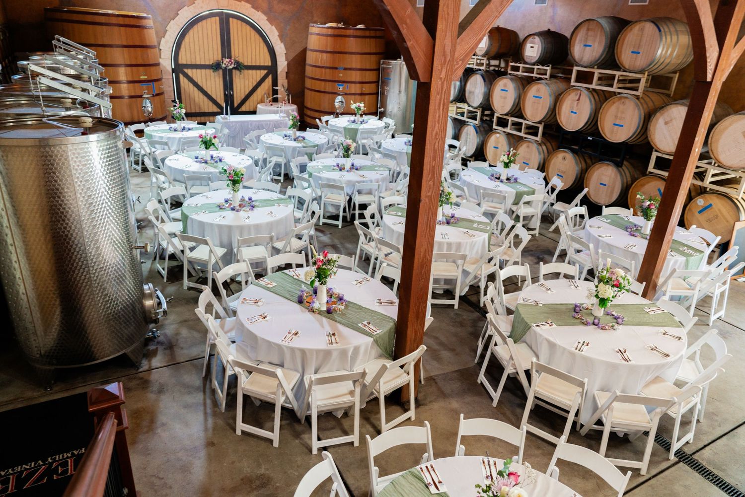 Elegant wedding reception tables set up in a rustic barn venue with wooden beams and barrels.
