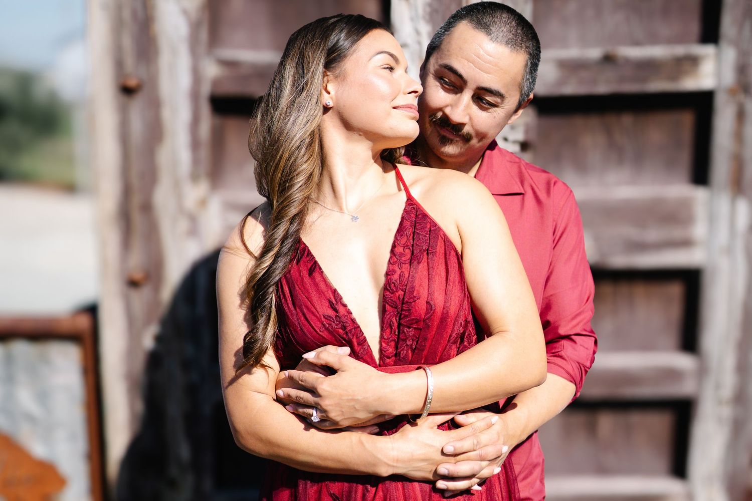Couple in matching red outfits embracing outdoors, woman in red dress smiling with eyes closed at Serendipity Cellars Winery