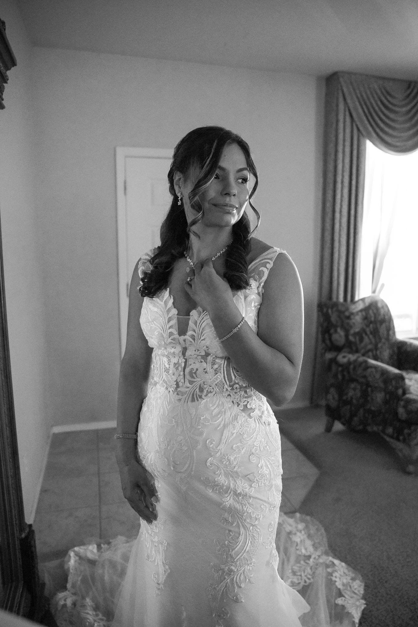 Bride in lace mermaid wedding gown adjusting jewelry in black and white photo.