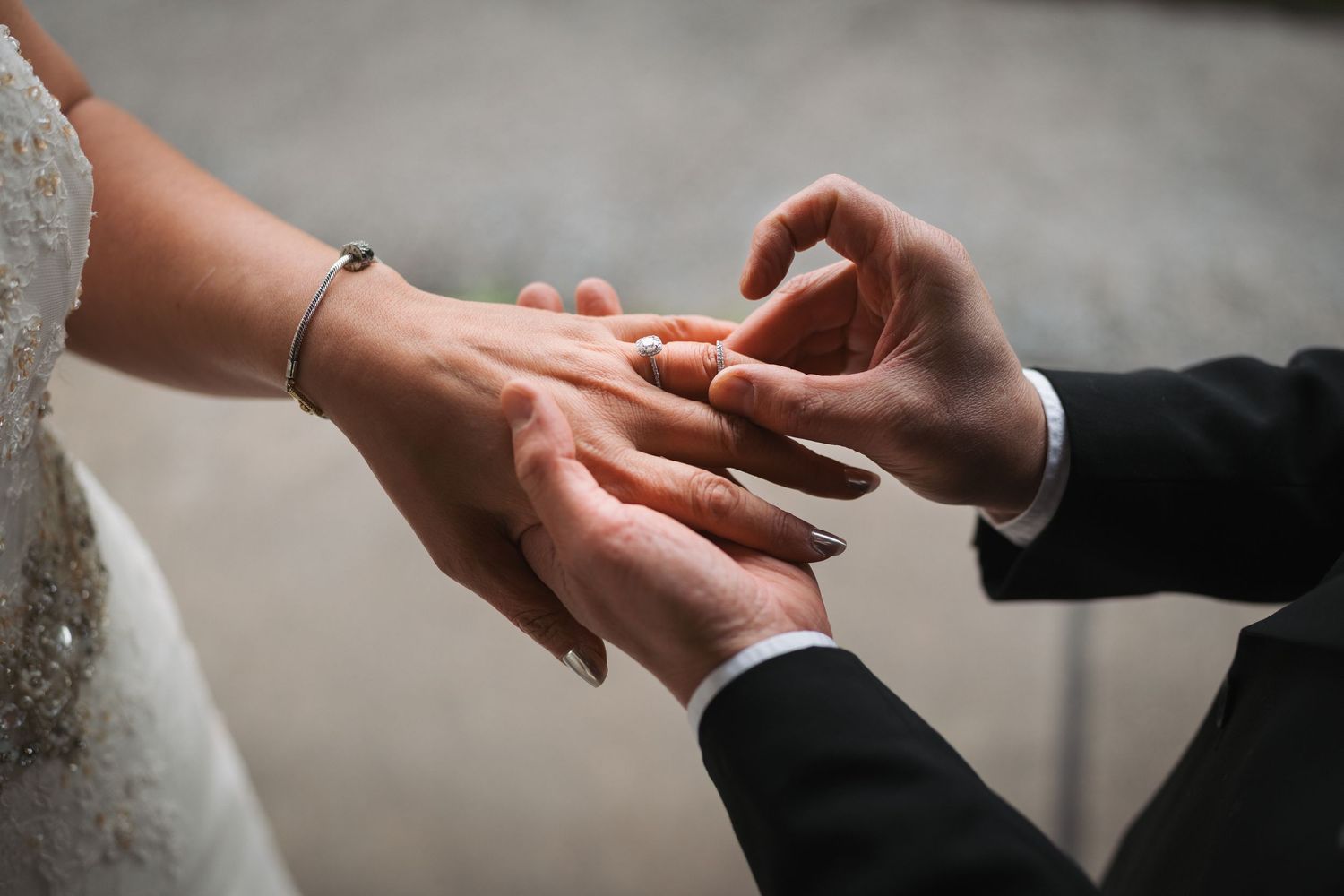 Groom placing a gold wedding ring on brides finger during wedding ceremony, close-up of hands.
