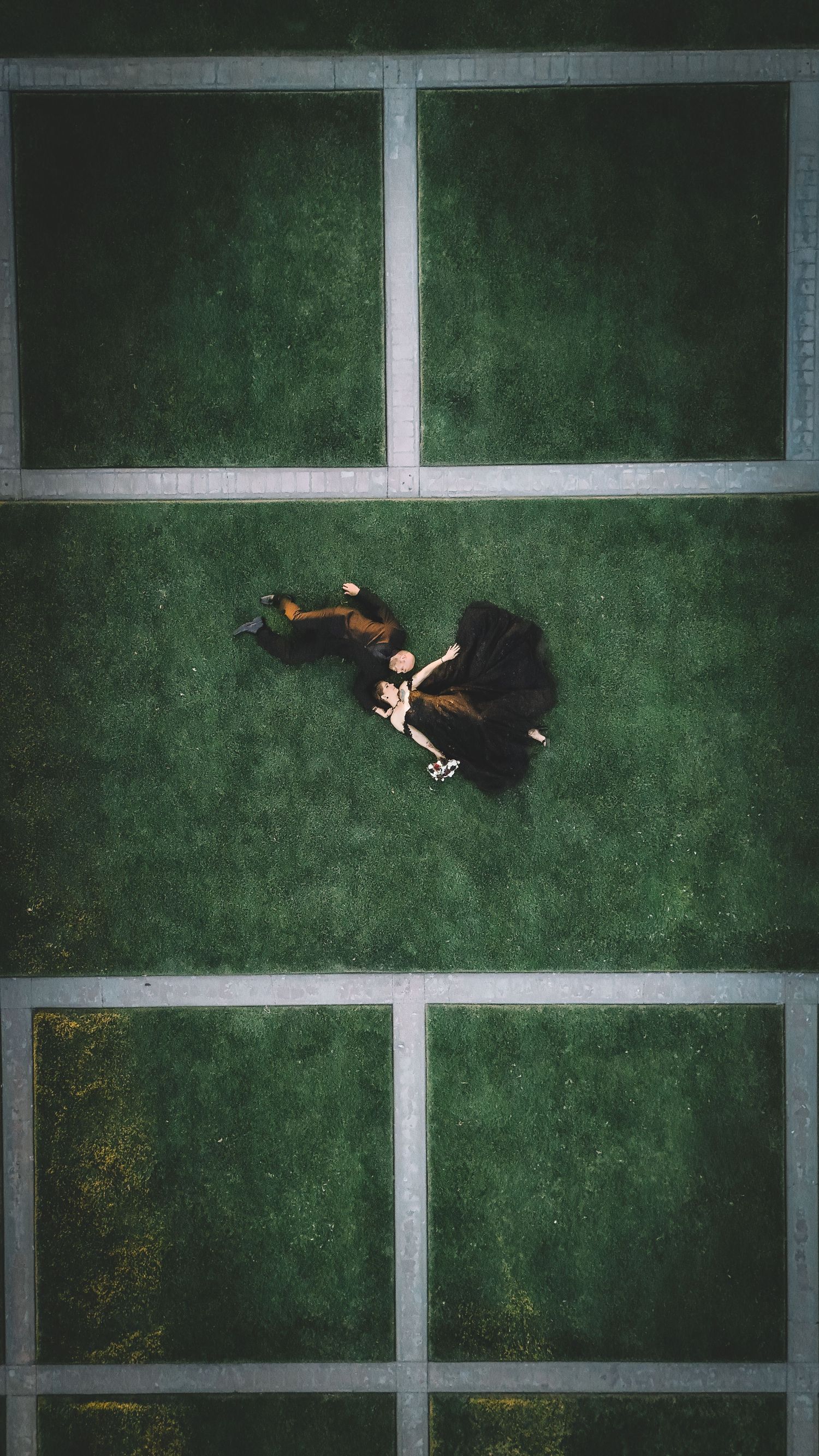 Aerial view of a person lying on geometric green sections divided by concrete paths.