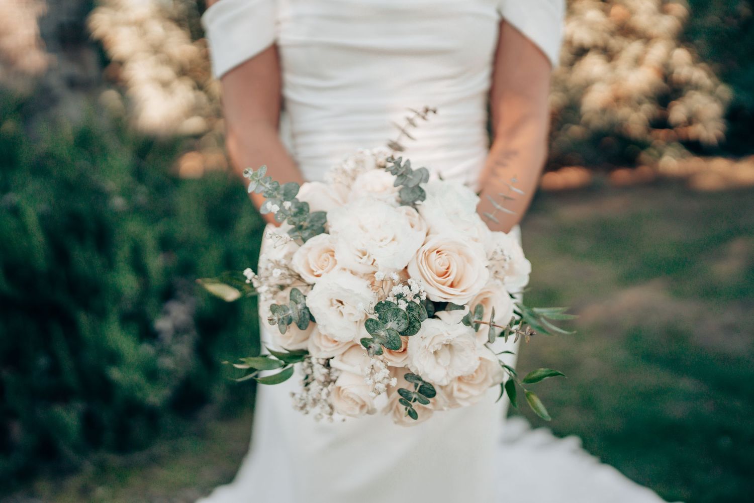 Bride holding elegant white and cream rose bouquet with eucalyptus greenery on her wedding day.