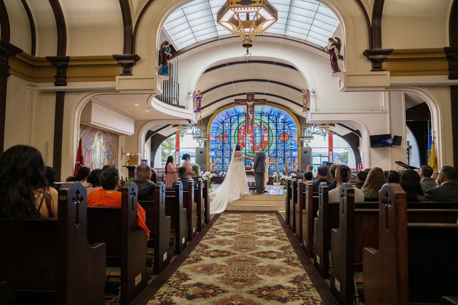 Interior of a grand church with wooden pews and stained glass windows illuminated by natural light.