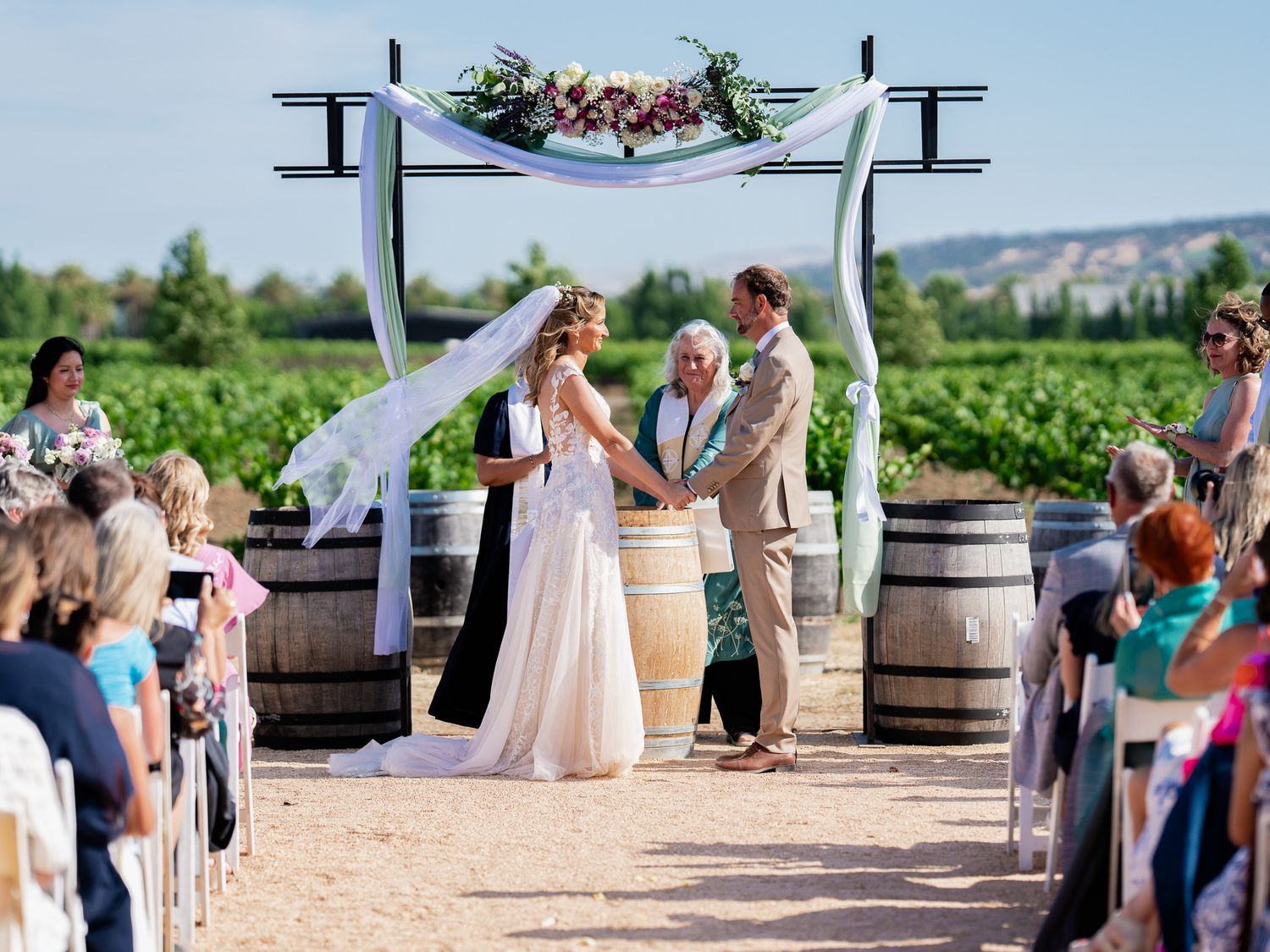 Outdoor vineyard wedding ceremony with rows of white chairs and wine barrels at Vezér Family Vineyard - Blue Victorian