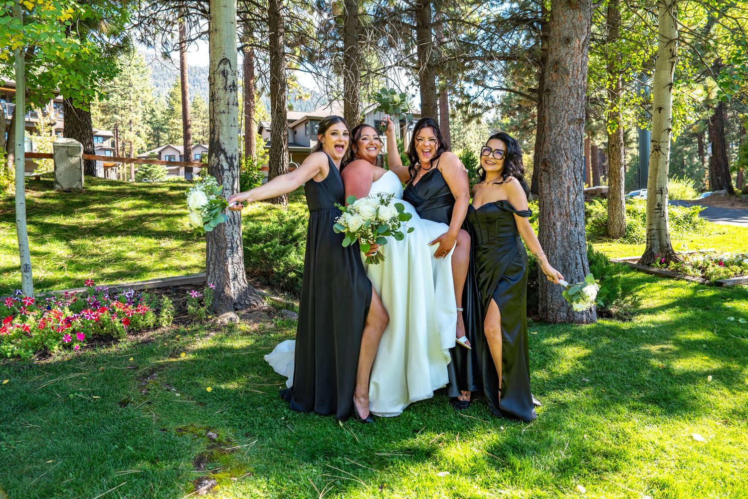 Wedding party gathered on sunny lawn with pine trees and green landscaping at Forest Suits Resorts