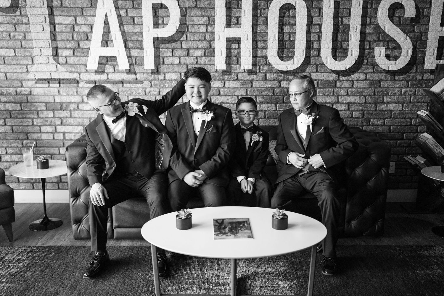 Groom and groomsmen in suits relaxing on a couch at a tap house venue in a black and white wedding photo.
