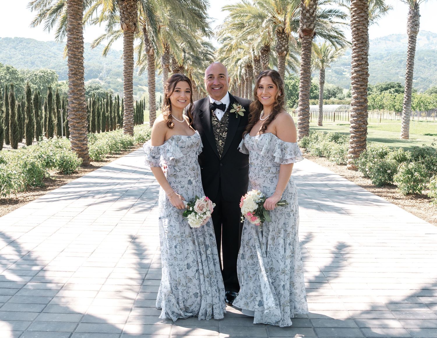 Wedding party poses on a palm-lined path in coordinated formal attire.