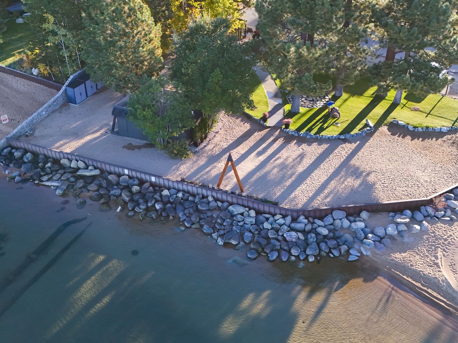 Aerial view of a beach shoreline with rocks and trees casting long shadows in Tahoe