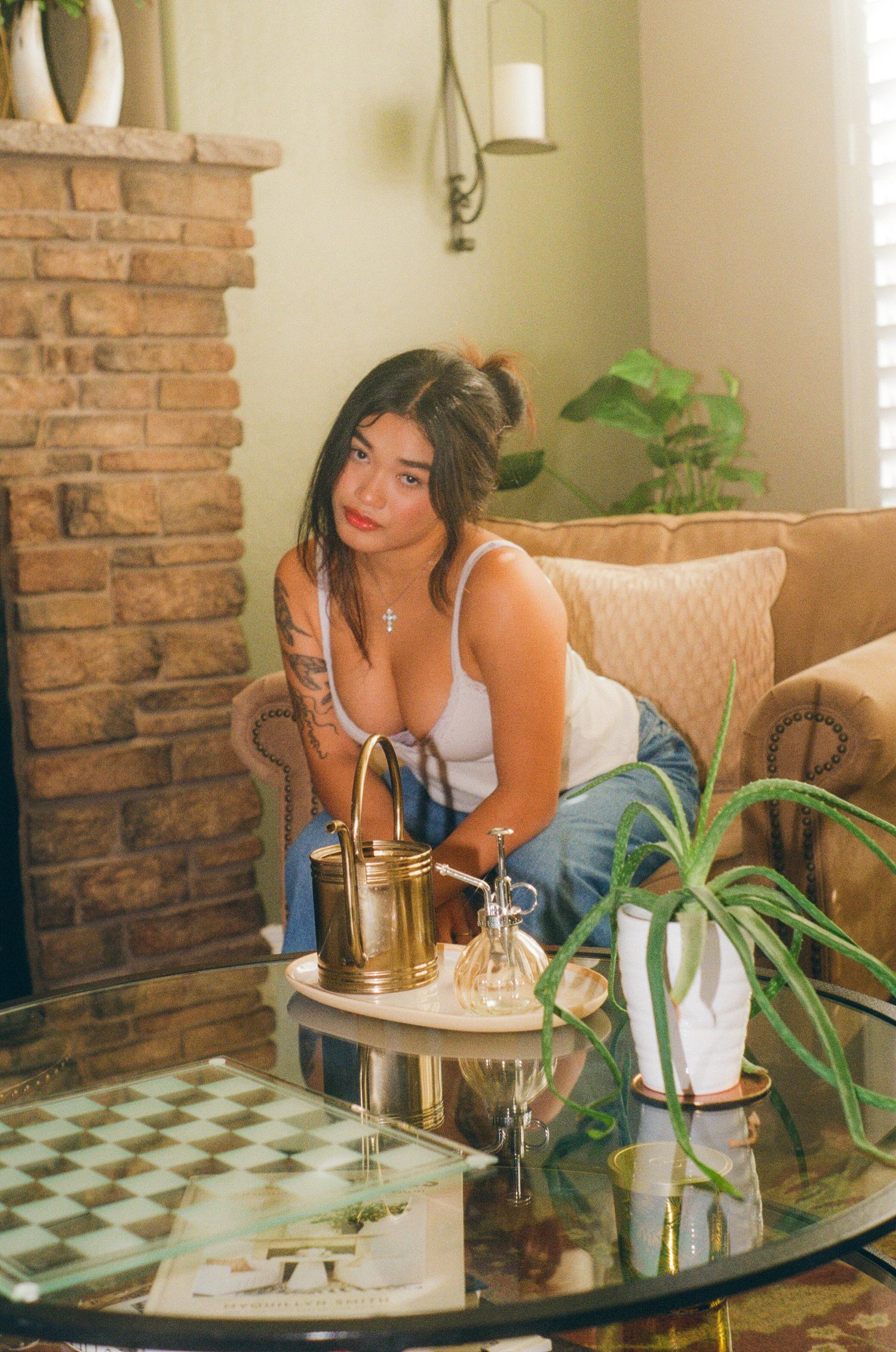 Woman in white tank top and jeans sitting by a glass coffee table in a cozy living room.