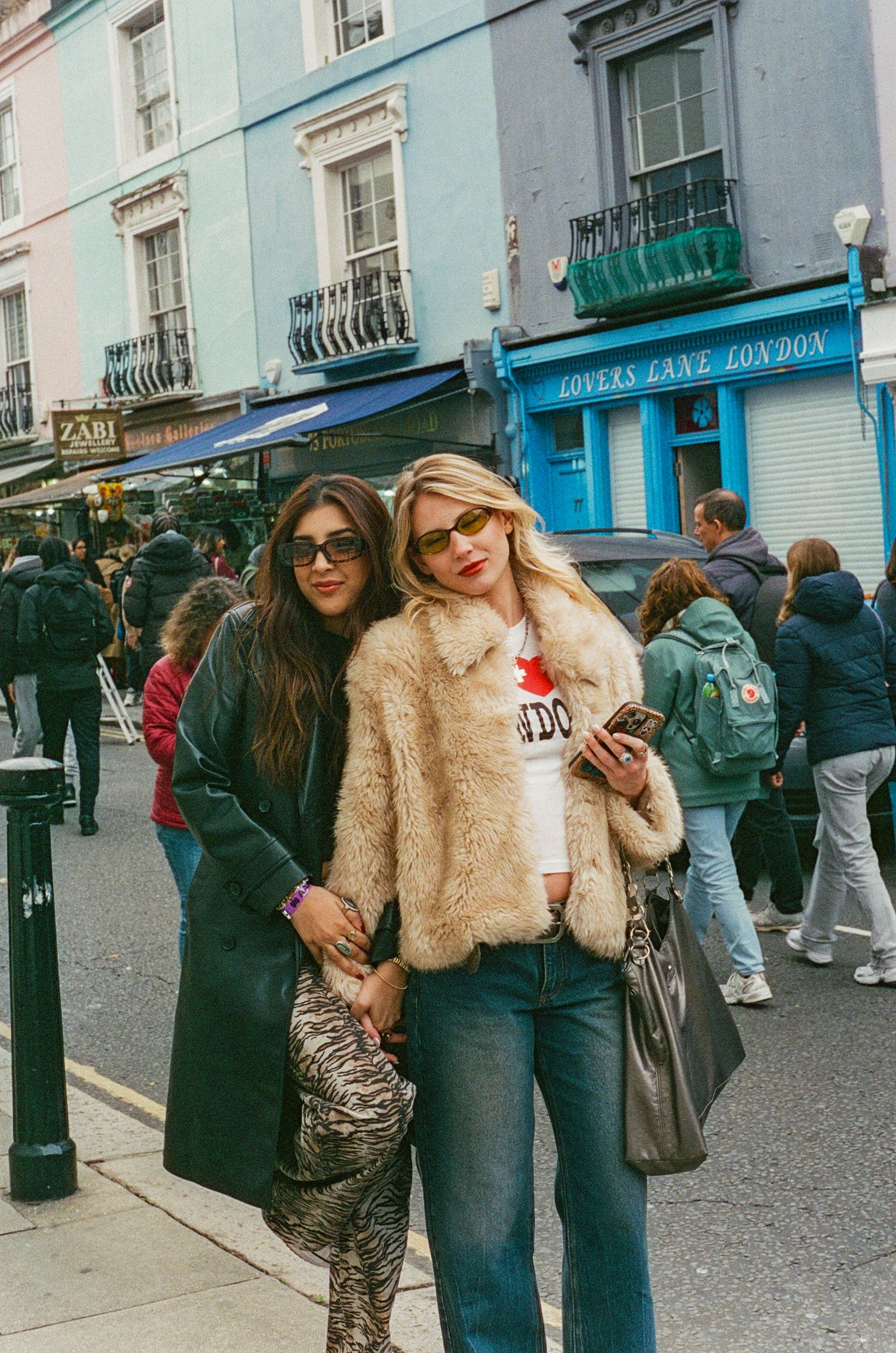 Two women posing on a busy London street near Lovers Lane London shop in stylish outfits.