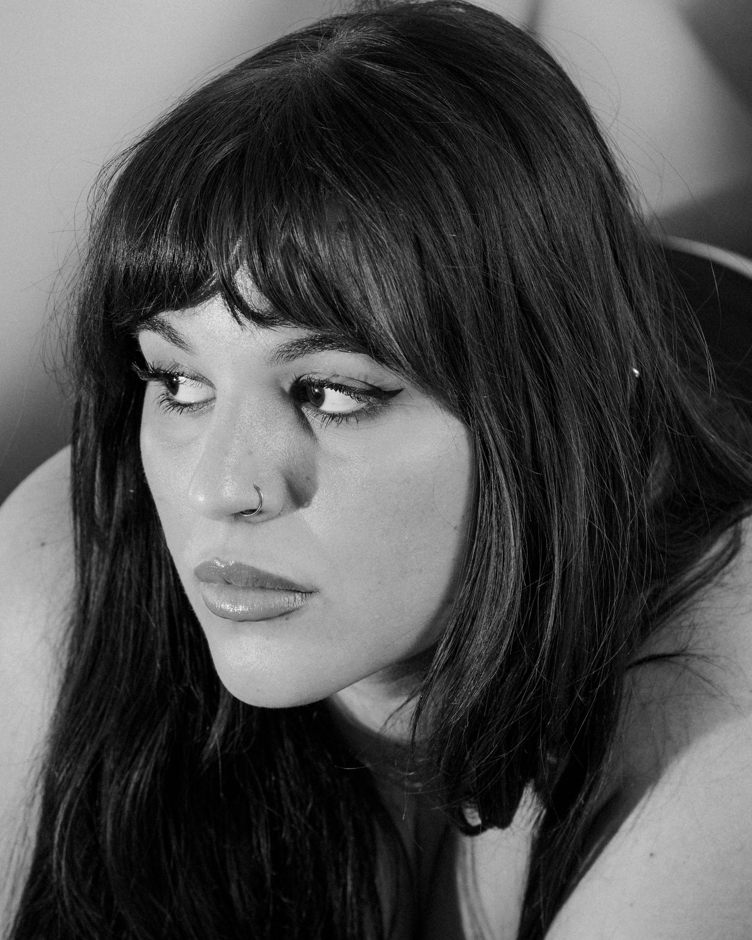 Black and white close-up portrait of a young woman with bangs and nose ring.