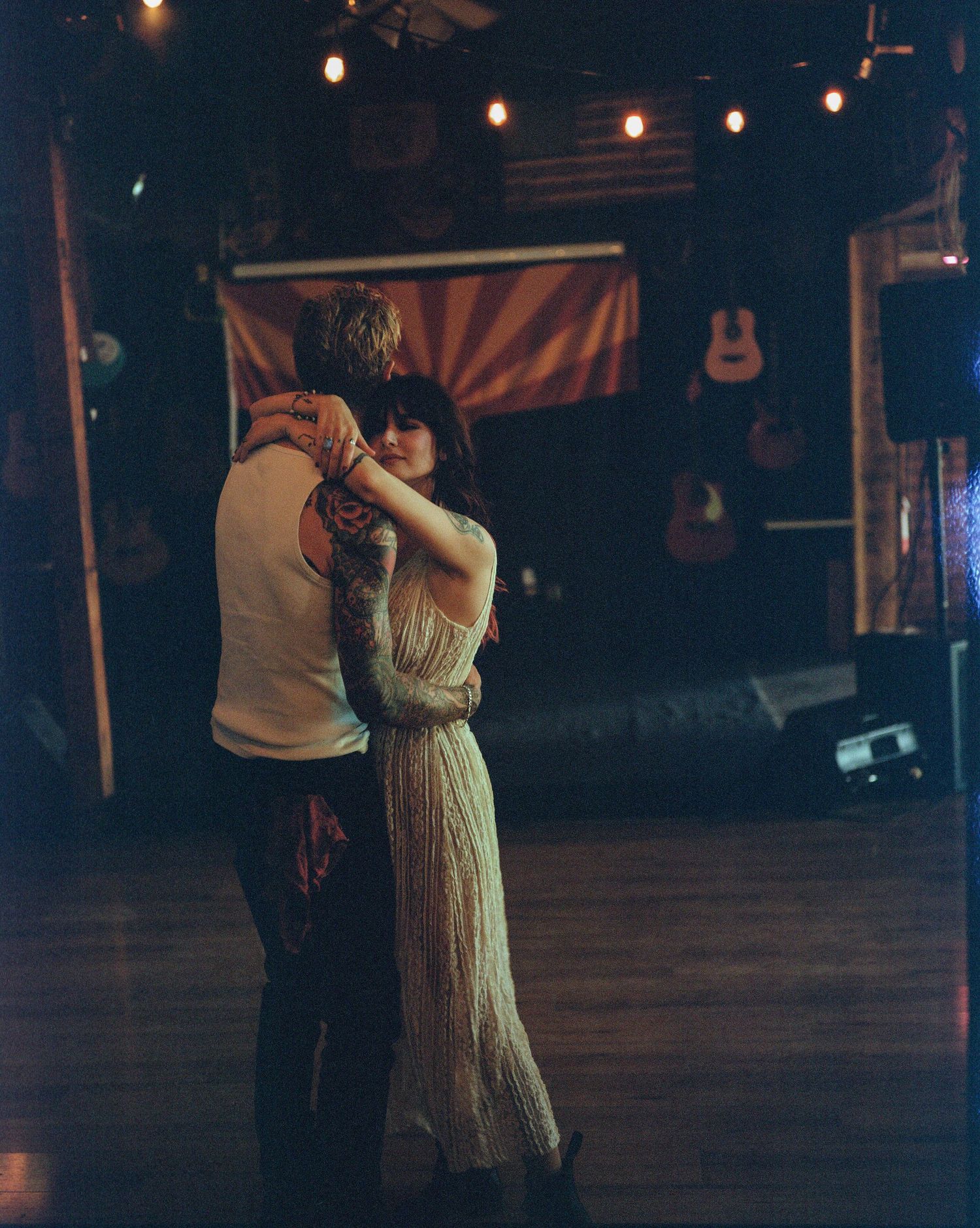 Couple slow dancing romantically in a dimly lit venue with string lights and guitars on the wall. From 'Dead Ends' music video