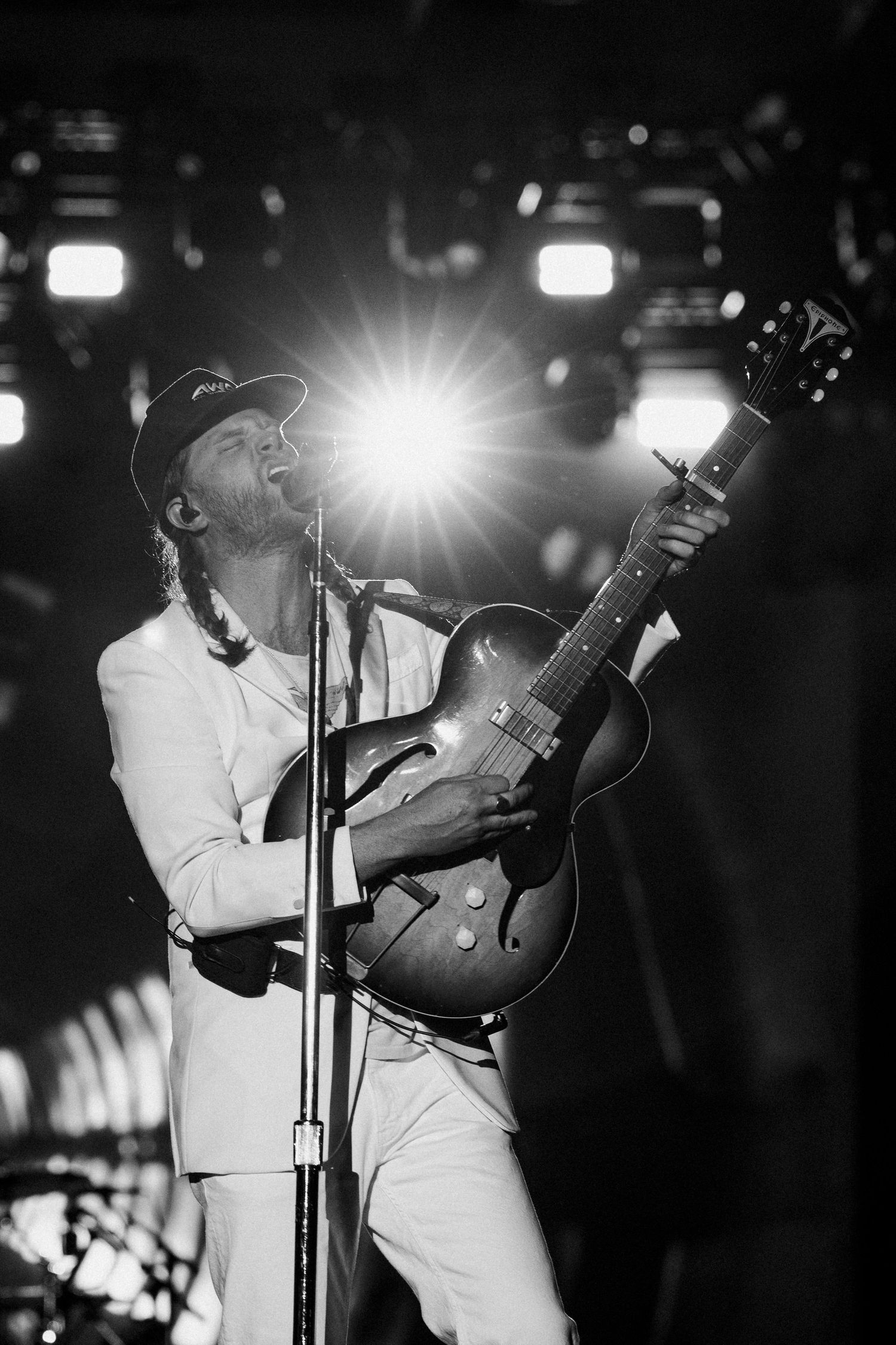 Black and white photo of guitarist in white suit passionately playing acoustic guitar under bright stage lights.