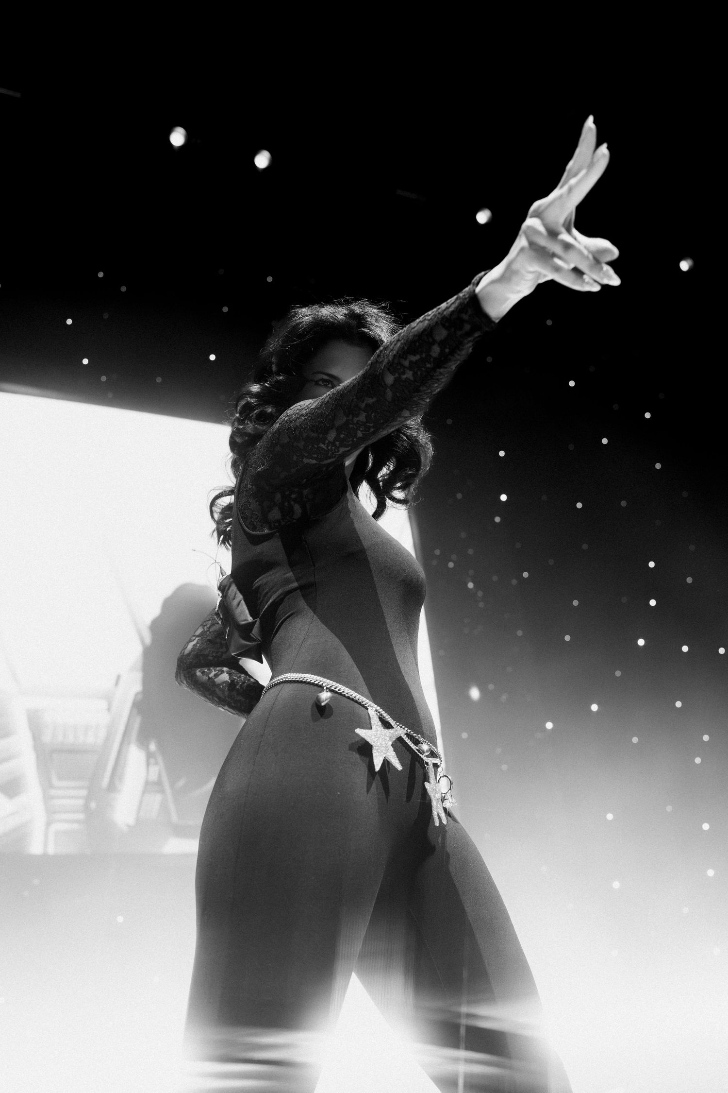 Black and white photo of a woman in a star-adorned bikini striking a dramatic pose on a lit stage.