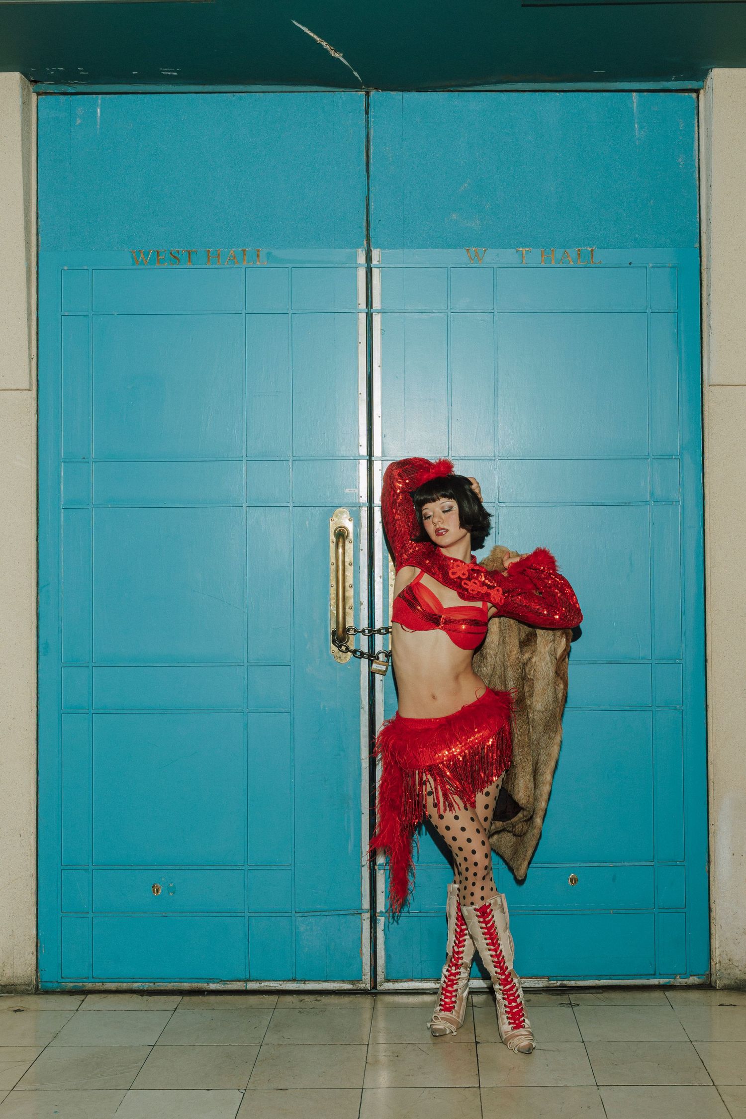 A burlesque performer in a red sequined costume poses against turquoise double doors.