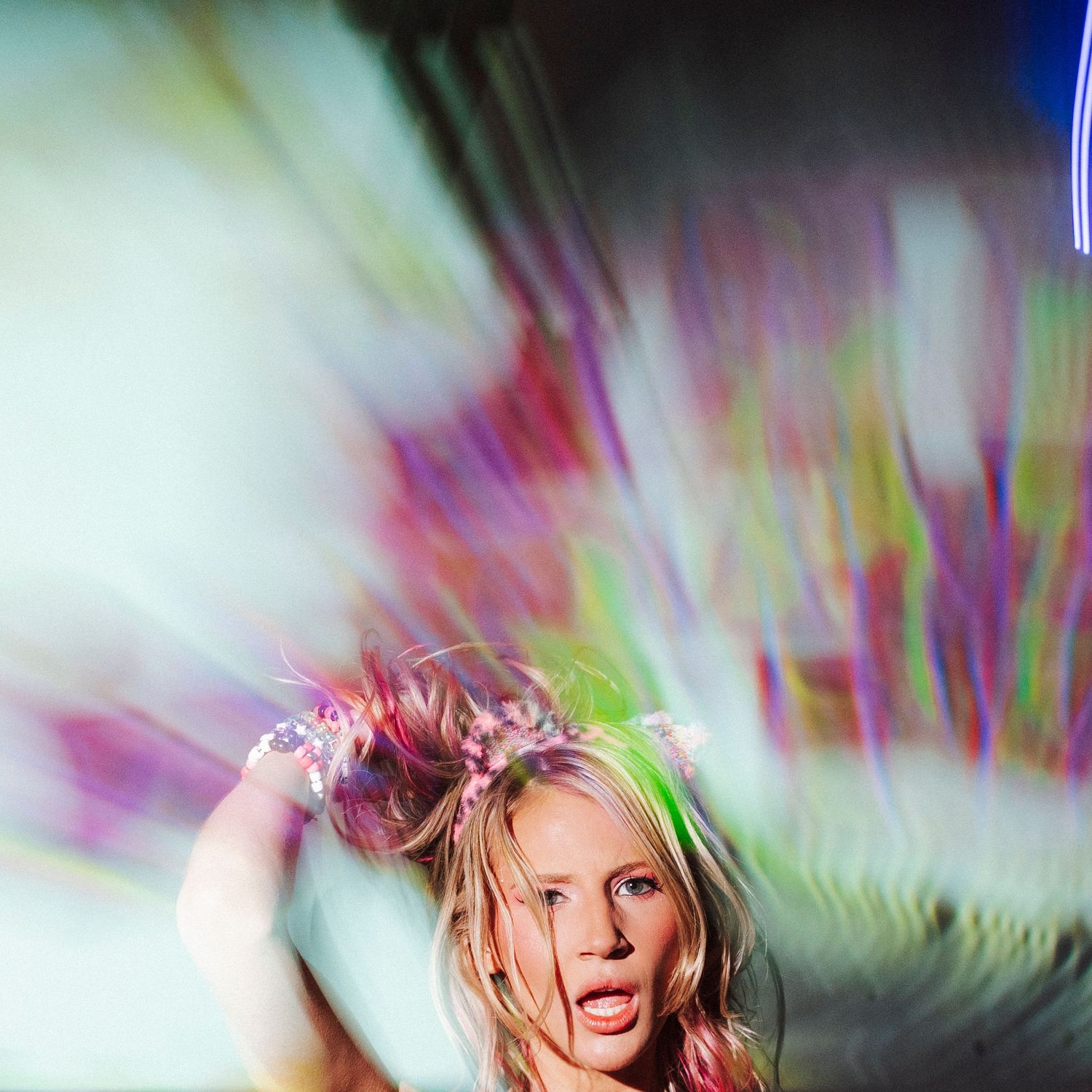 Blonde woman with a floral crown surrounded by colorful motion-blurred light streaks at a festival.