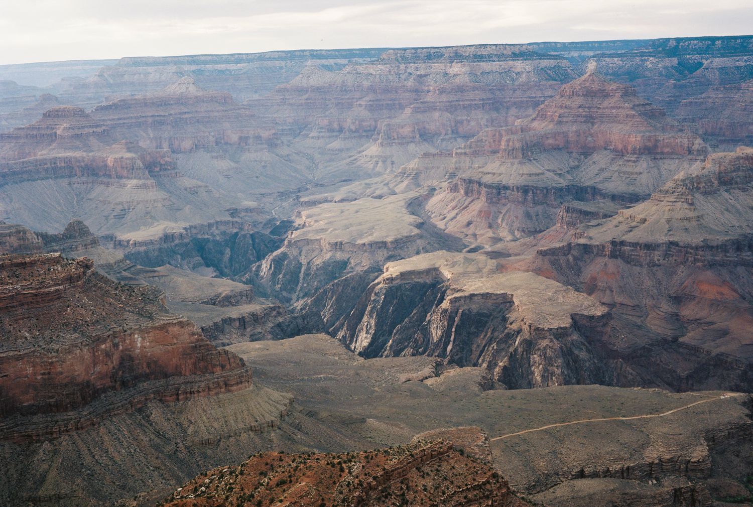 Aerial view of the Grand Canyon's layered red rock formations and deep gorges under a hazy sky.