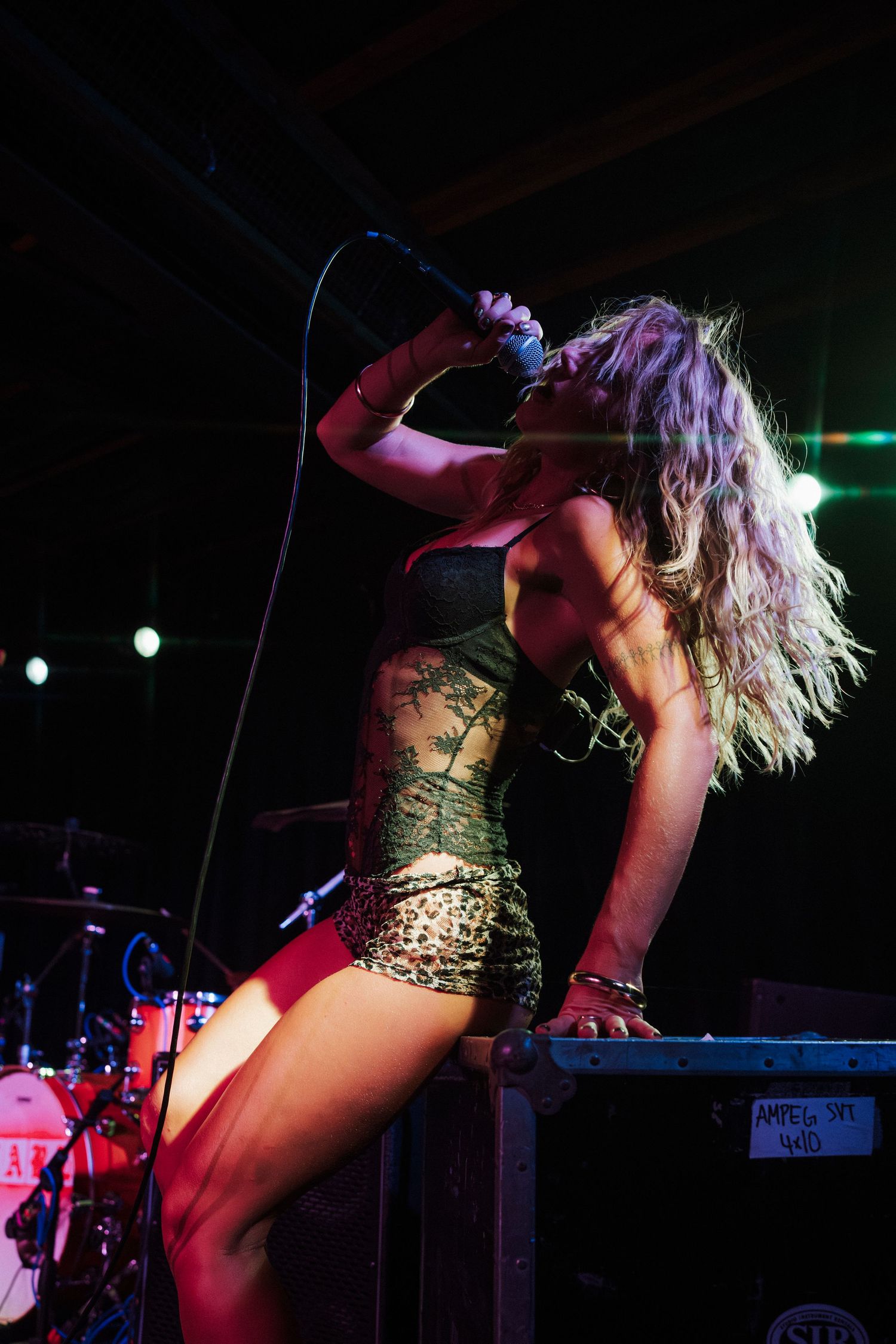 Female rock singer performing on stage, holding microphone, wearing crop top and leopard shorts with tattoos visible.