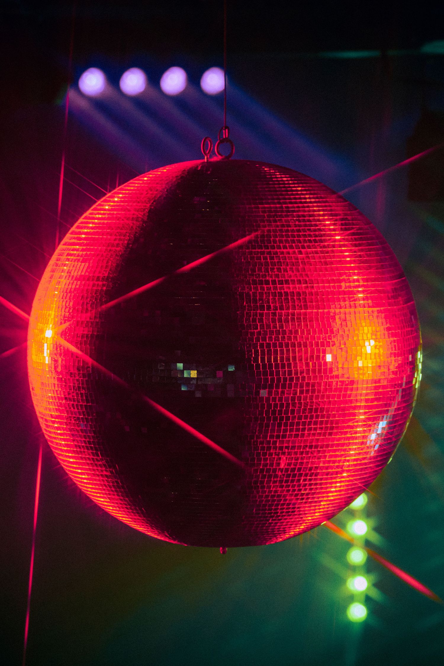 A glowing red disco mirror ball hanging from the ceiling with colorful stage lights in a dark nightclub.