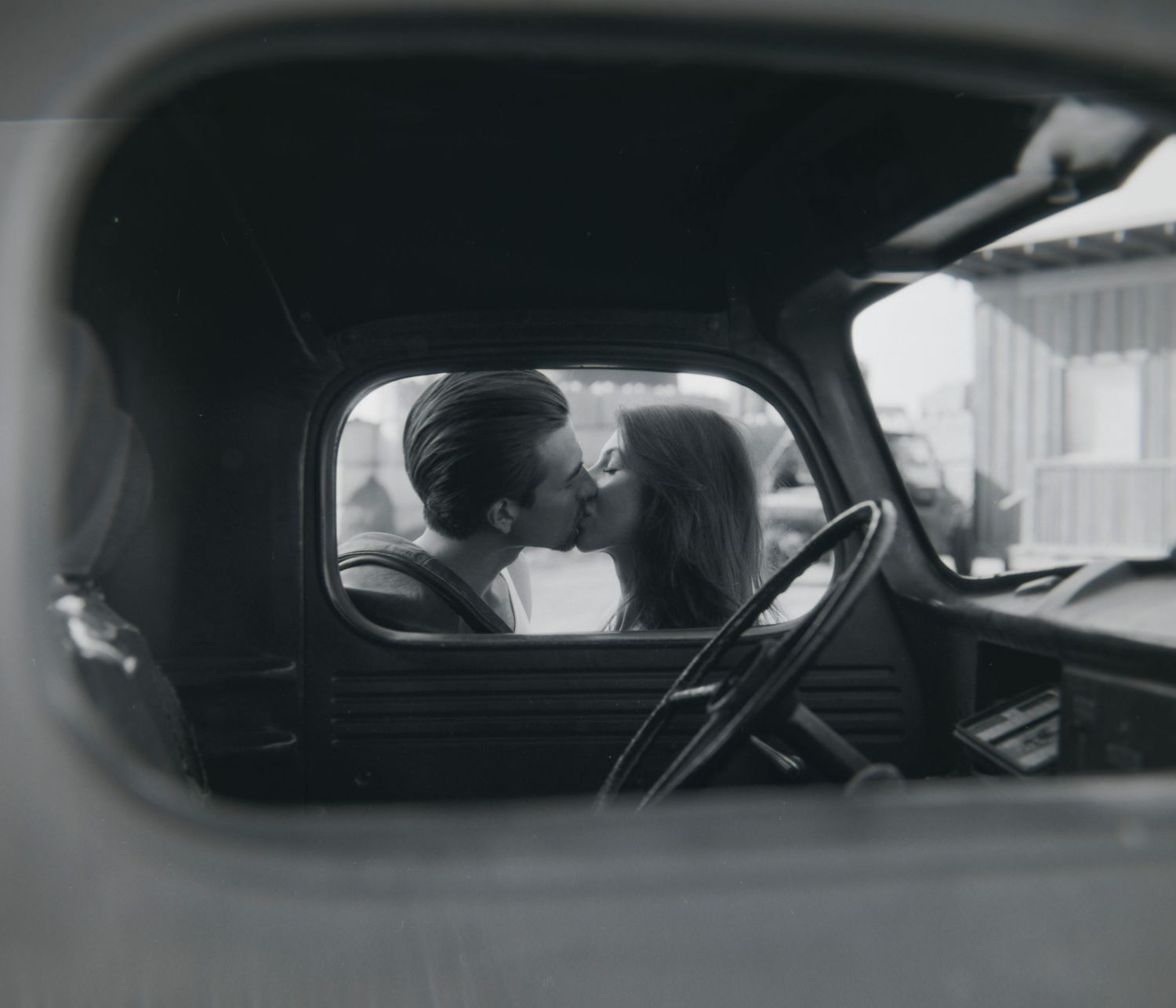 Black and white photo of a couple kissing inside a vintage truck cab.