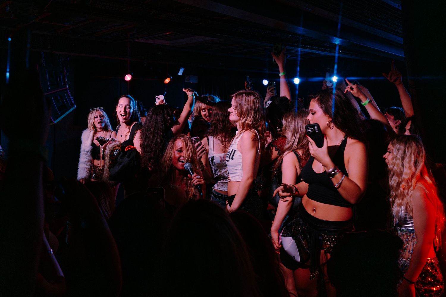 Group of women dancing and celebrating at a lively nightclub party under colorful stage lights.