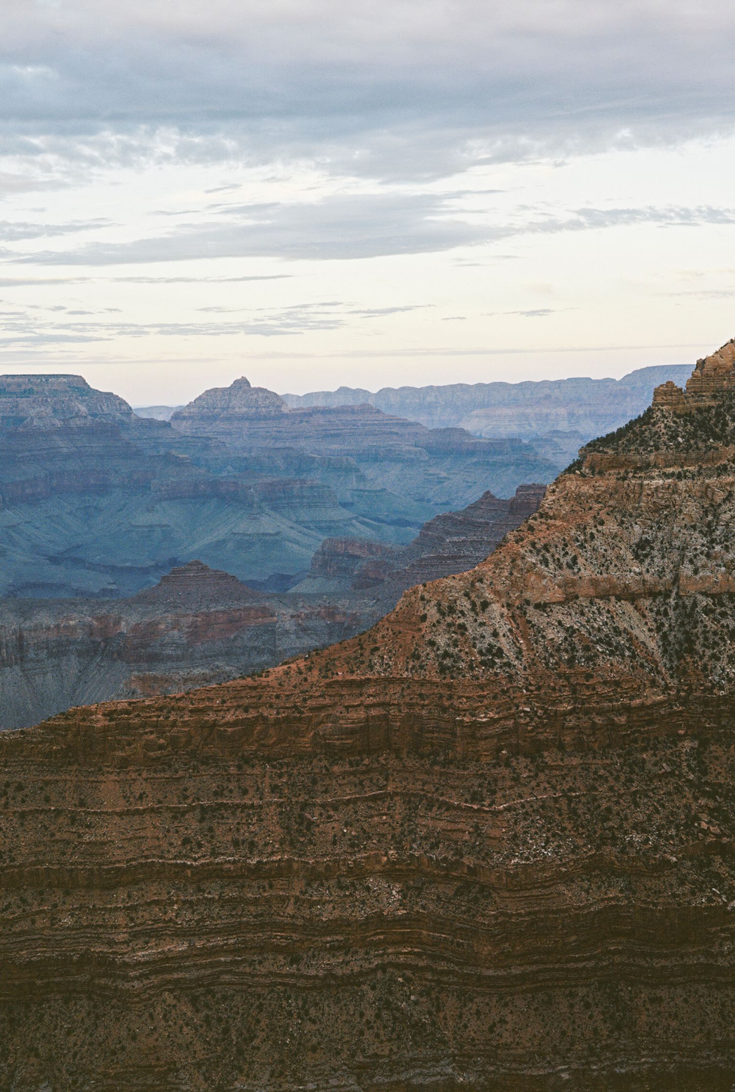 Stunning layered rock formations of the Grand Canyon at dusk with misty blue ridges receding into a cloudy sky.