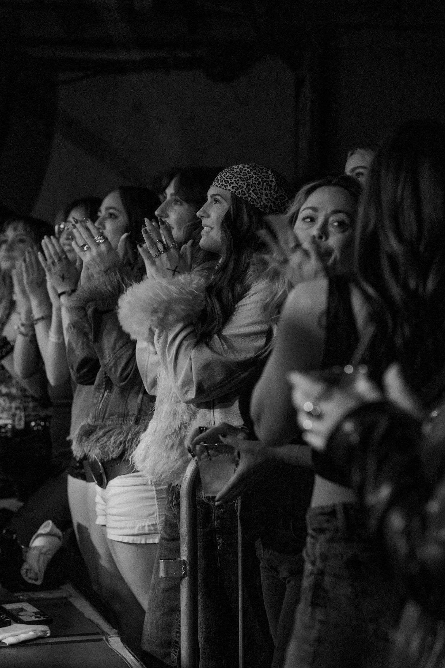 Black and white photo of enthusiastic female concert crowd clapping and cheering at live music venue.