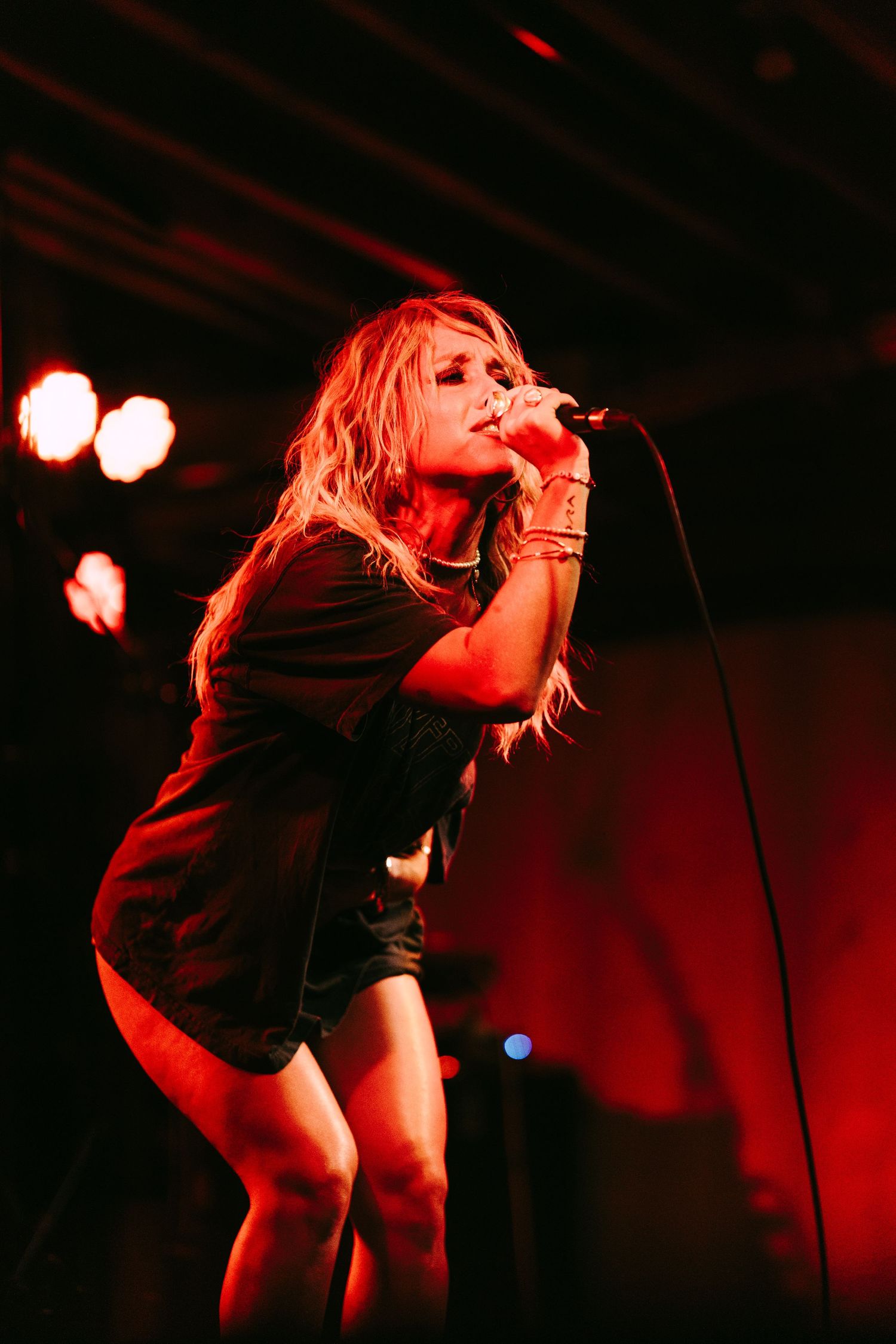 Blonde female singer performing on stage under red lights, holding microphone in black outfit at live concert. Pearl 2025