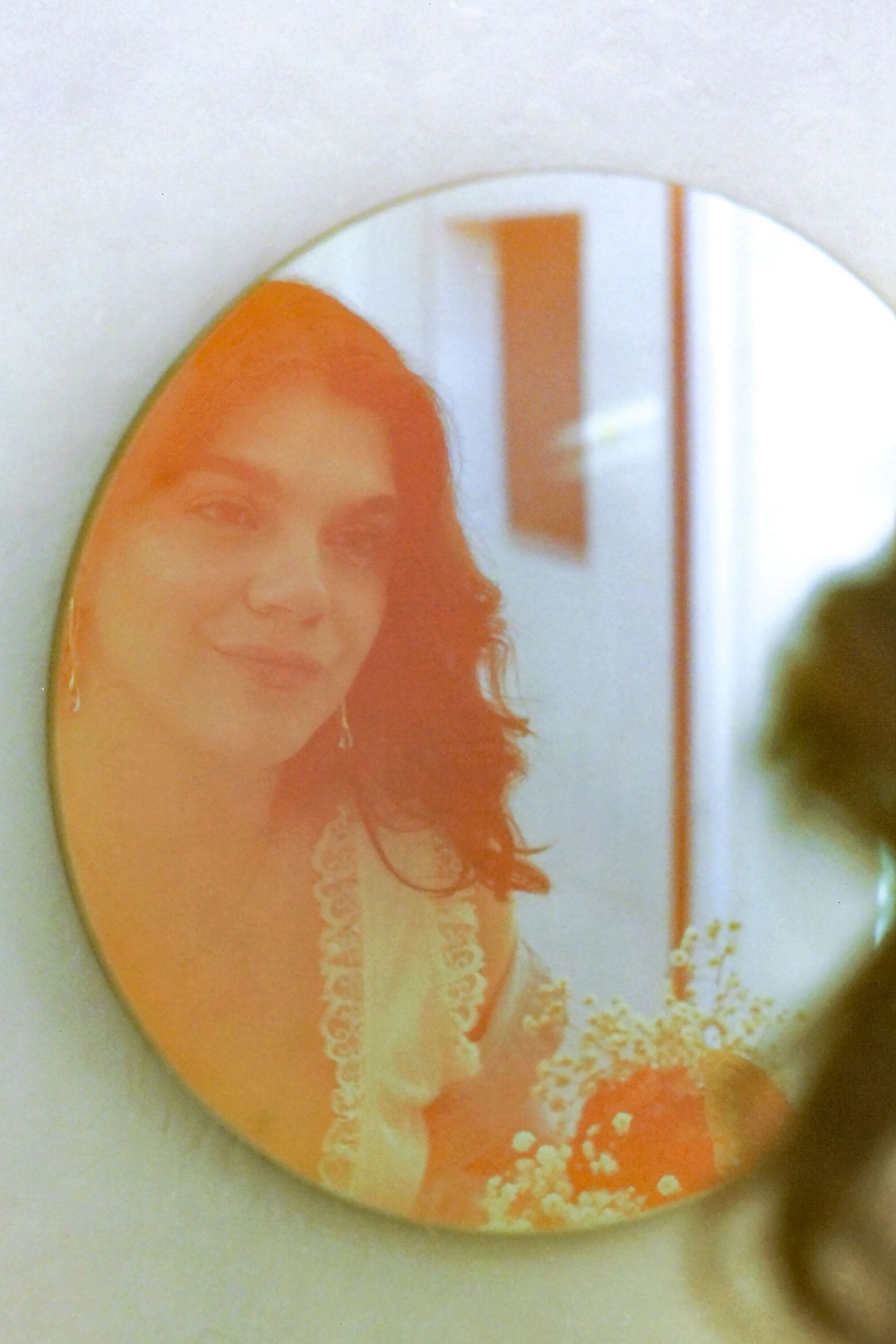 Woman with dark curly hair smiling in warm-toned circular mirror reflection.