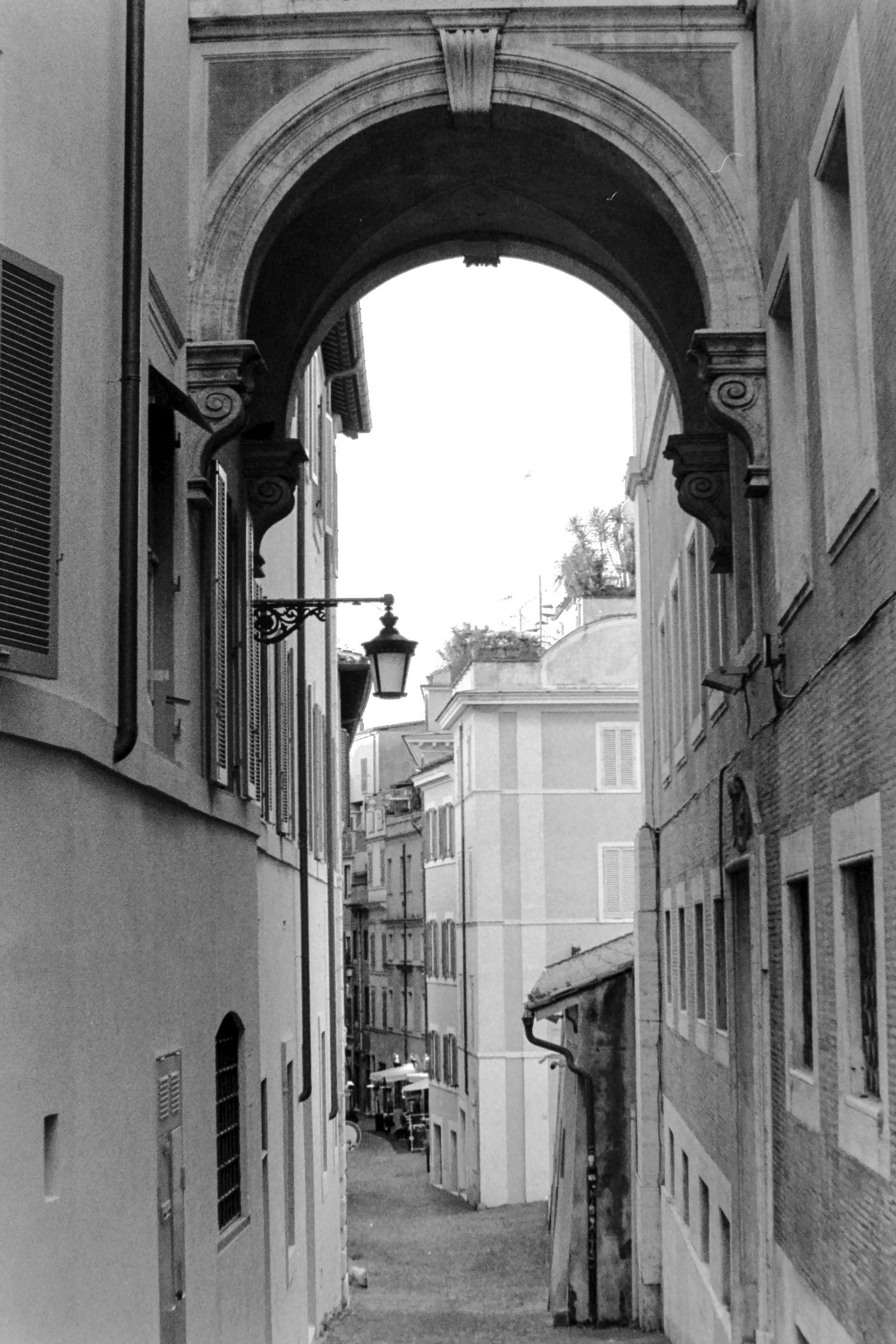 Black and white photo of narrow European alley viewed through ornate stone arch.