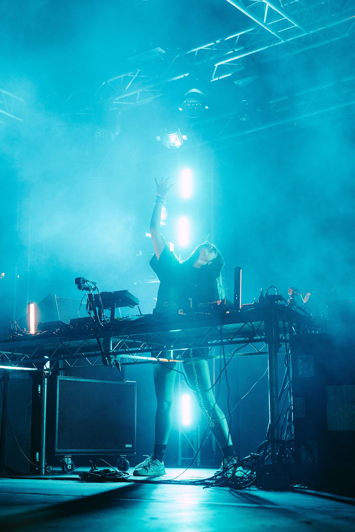 DJ performs on stage surrounded by teal smoke and dramatic concert lighting effects.