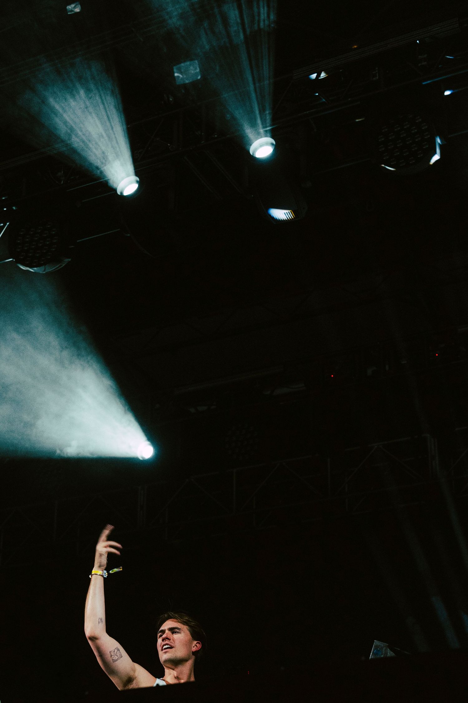 Low angle shot of performer raising hand on dark stage with dramatic beam lighting overhead.