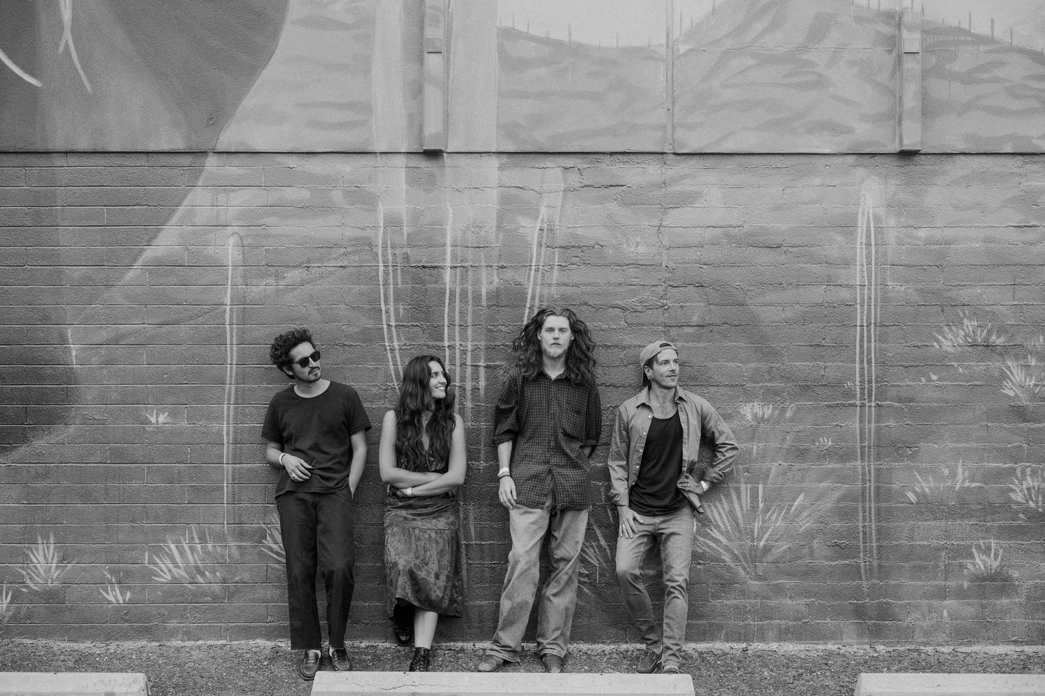 Four young adults pose against a mural-painted wall in a black and white outdoor photo.