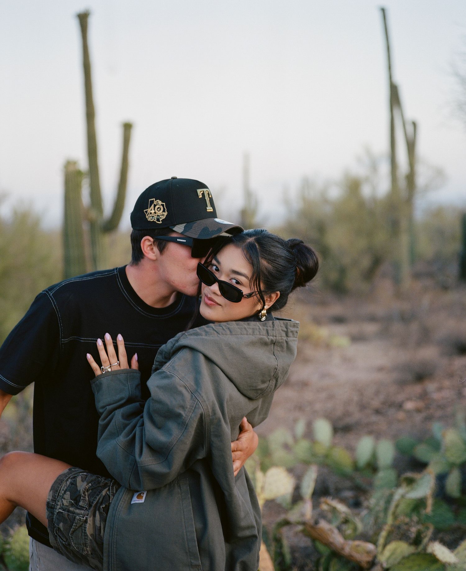 Couple sharing a kiss among saguaro cacti in Arizona desert at dusk.