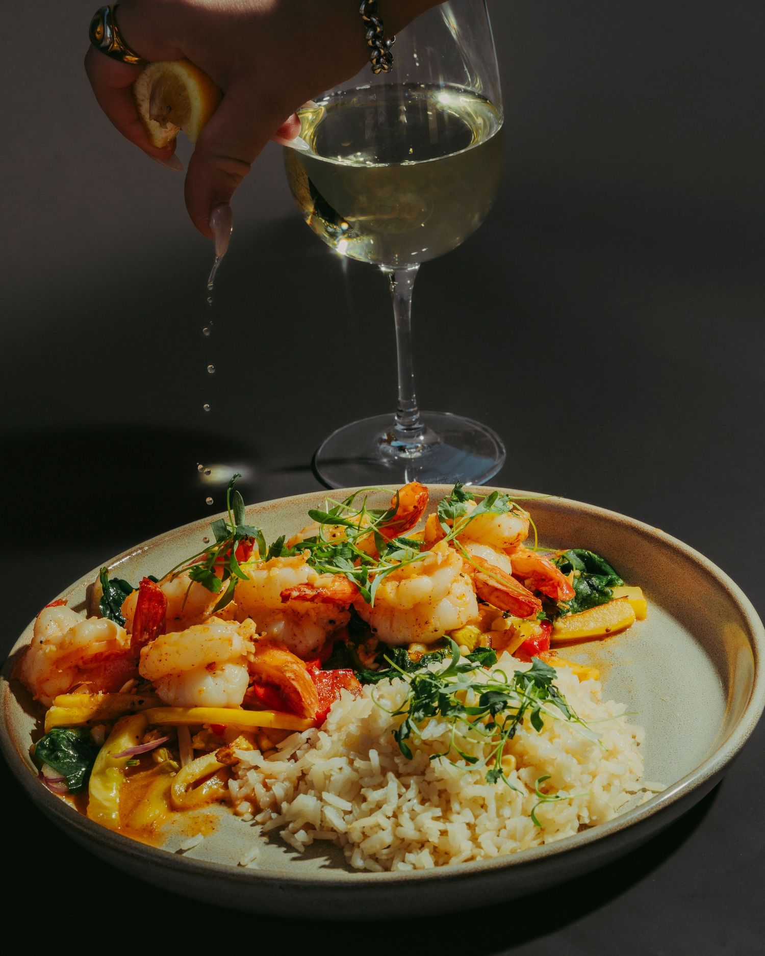 Shrimp dish with rice and greens as lemon juice is squeezed from a wine glass.