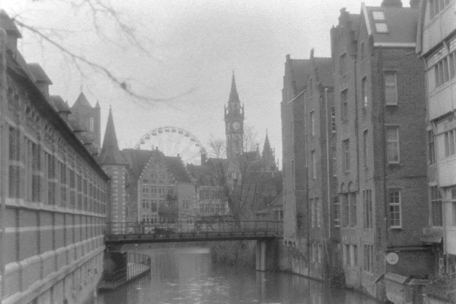 Black and white canal view in Ghent with a Ferris wheel and historic buildings reflected in calm water.