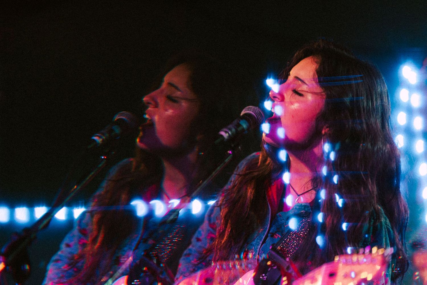 Two female musicians perform on stage with colorful LED lights in their hair at a live concert.