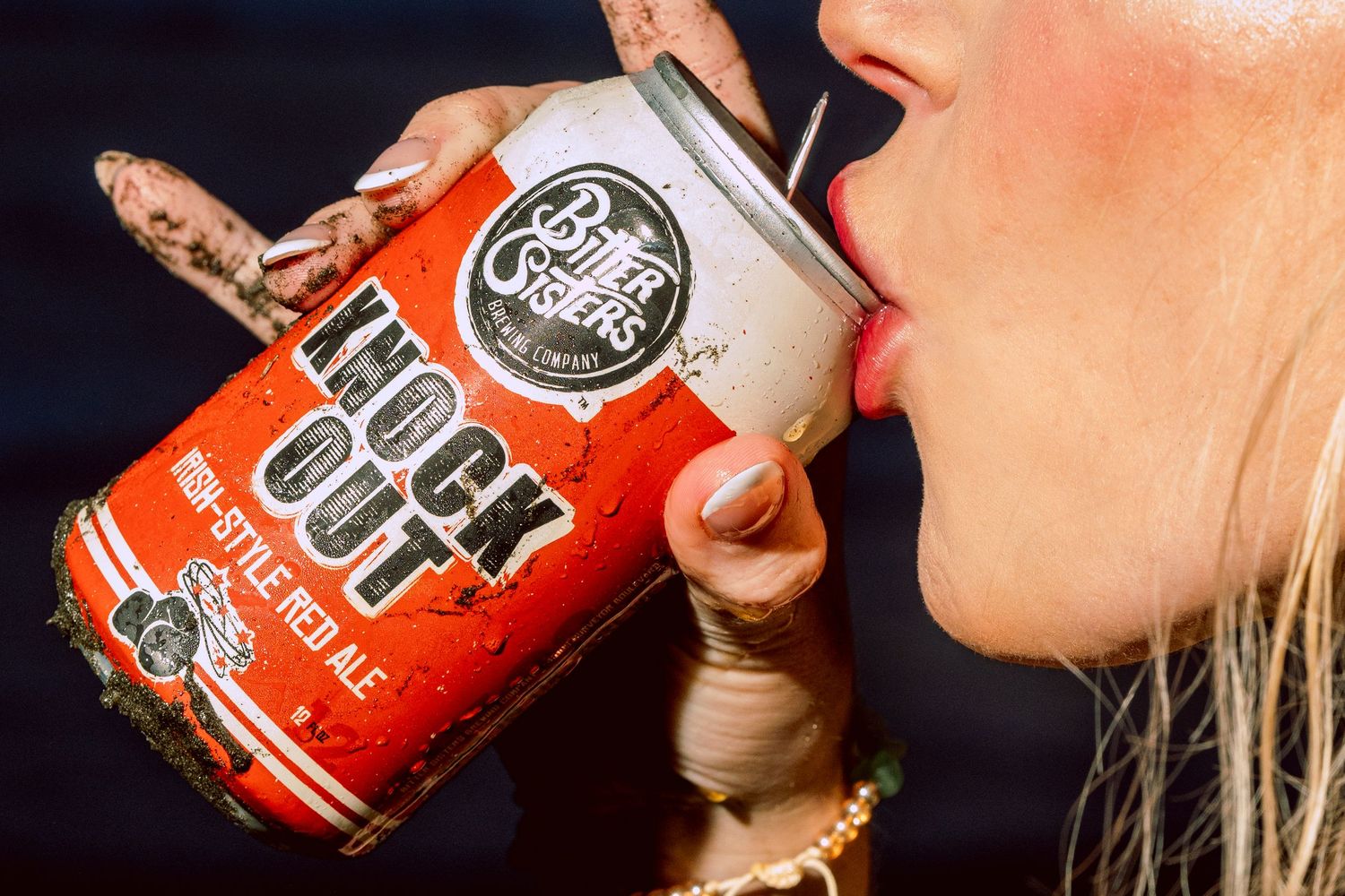 Woman drinking Pete's Crafts Knock Out Irish-Style Red Ale from a muddy can outdoors.
