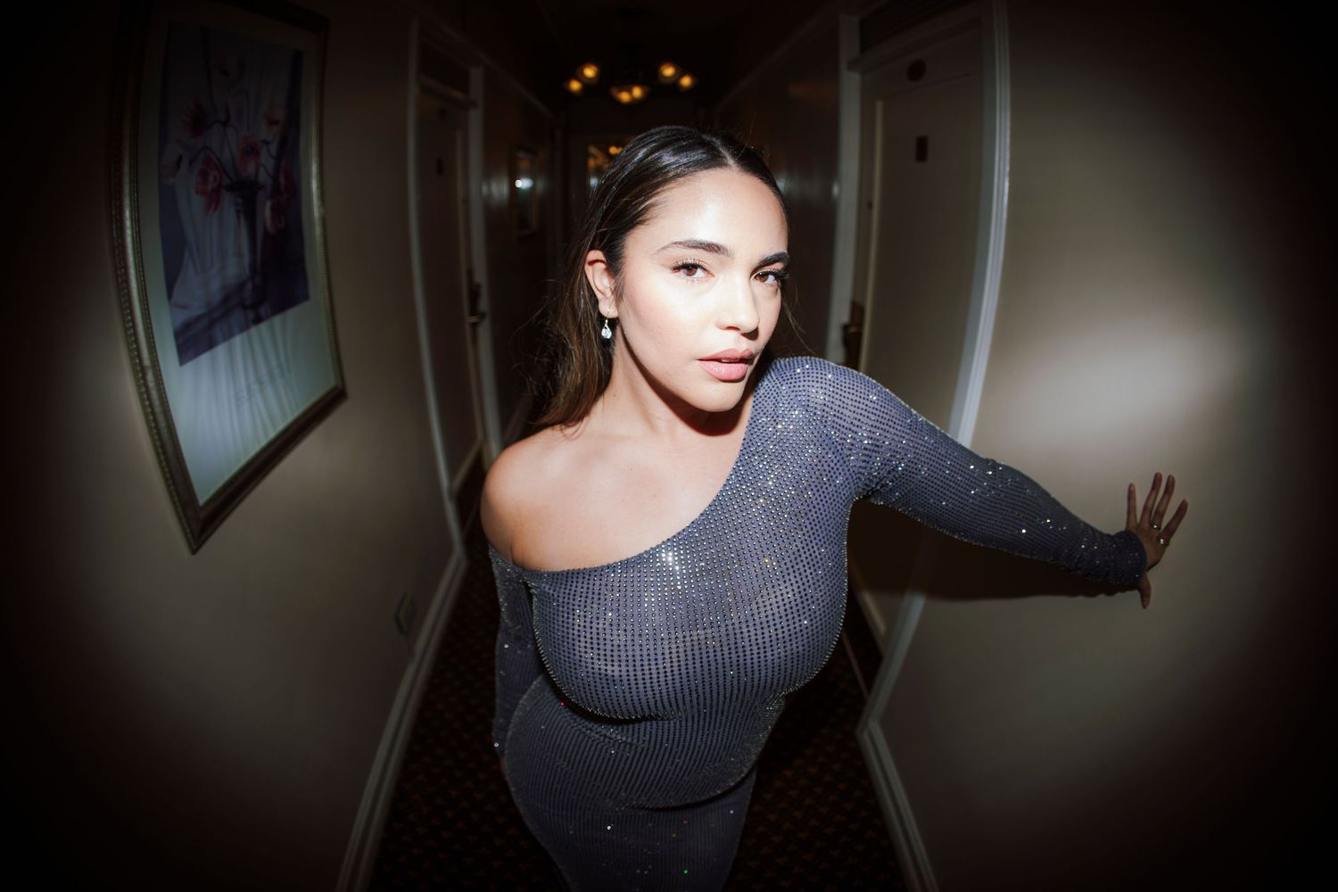 Young woman in sparkly grey dress posing in hotel corridor.