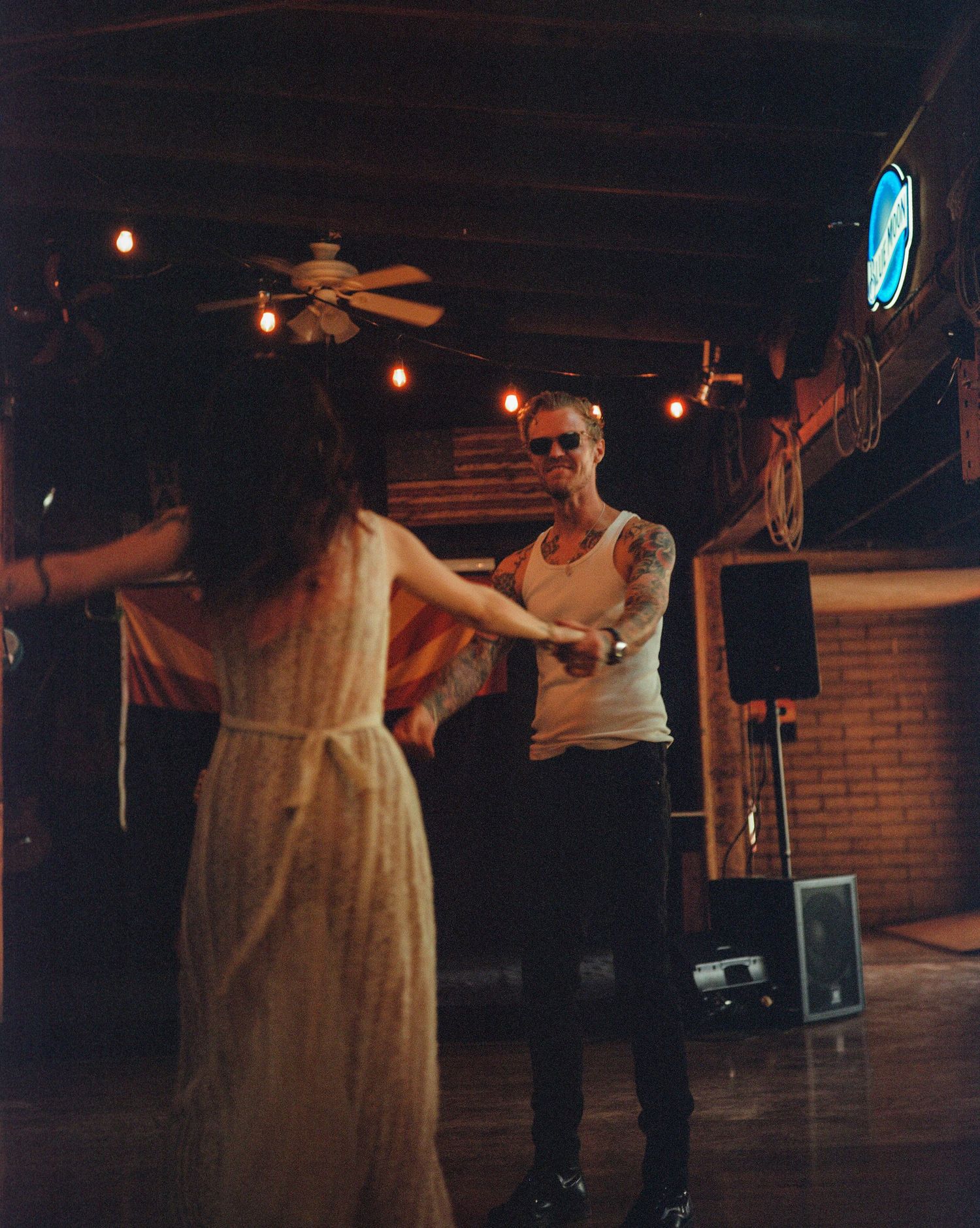 Two people dancing together in a dimly lit rustic bar with warm string lights and a ceiling fan overhead. From 'Dead Ends' music video