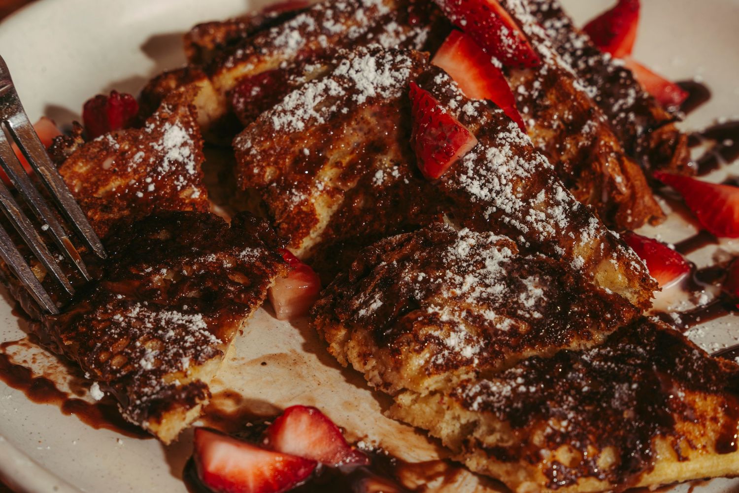 Close-up of French toast with fresh strawberries and chocolate sauce on a plate.
