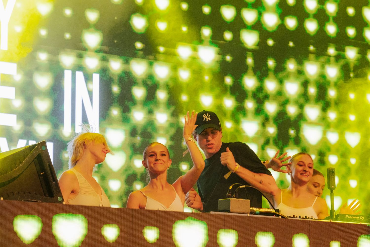 DJ and three women performing together on stage with bright yellow heart-shaped LED backdrop.