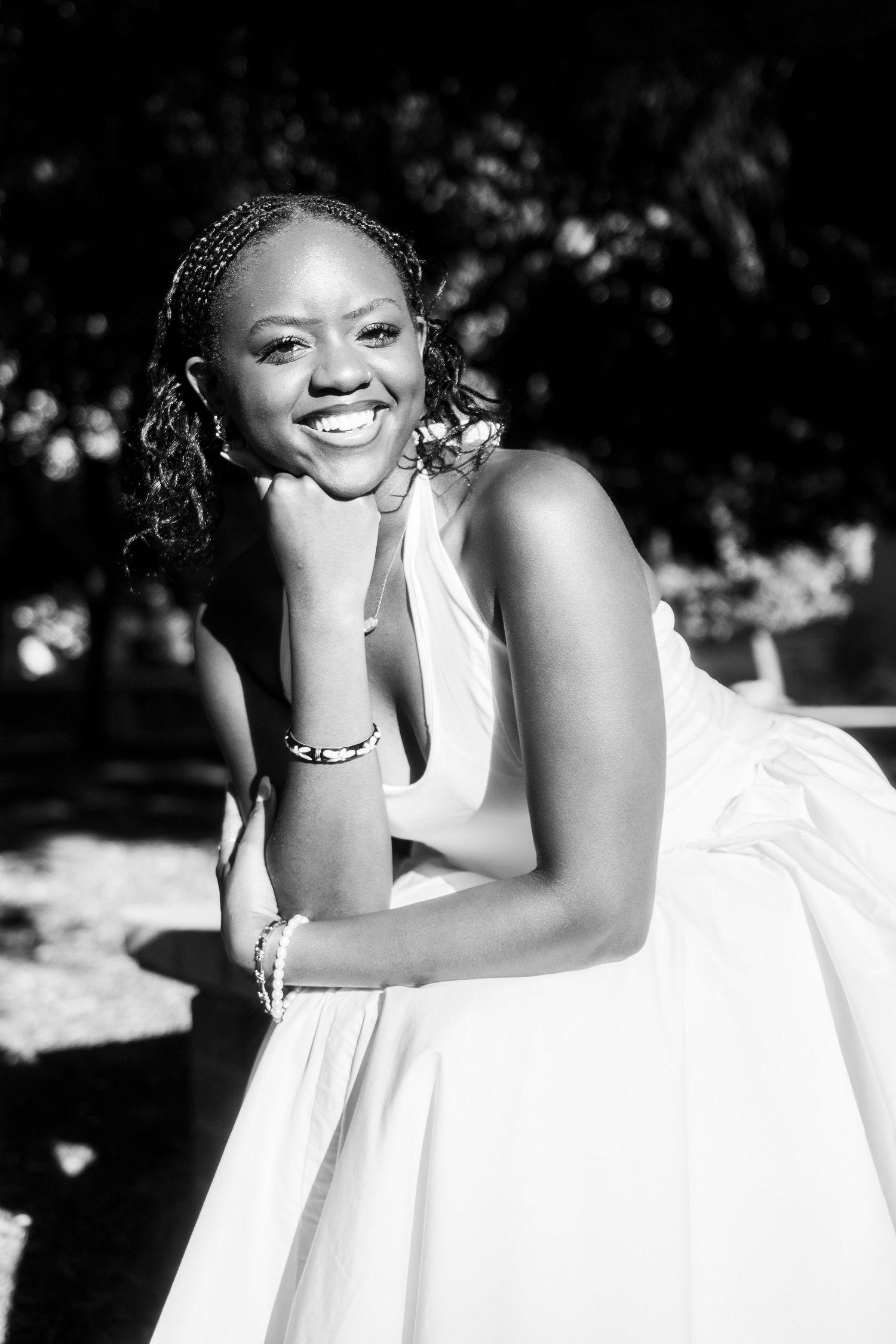 Smiling young Black woman in white halter dress poses outdoors in black and white portrait photo.